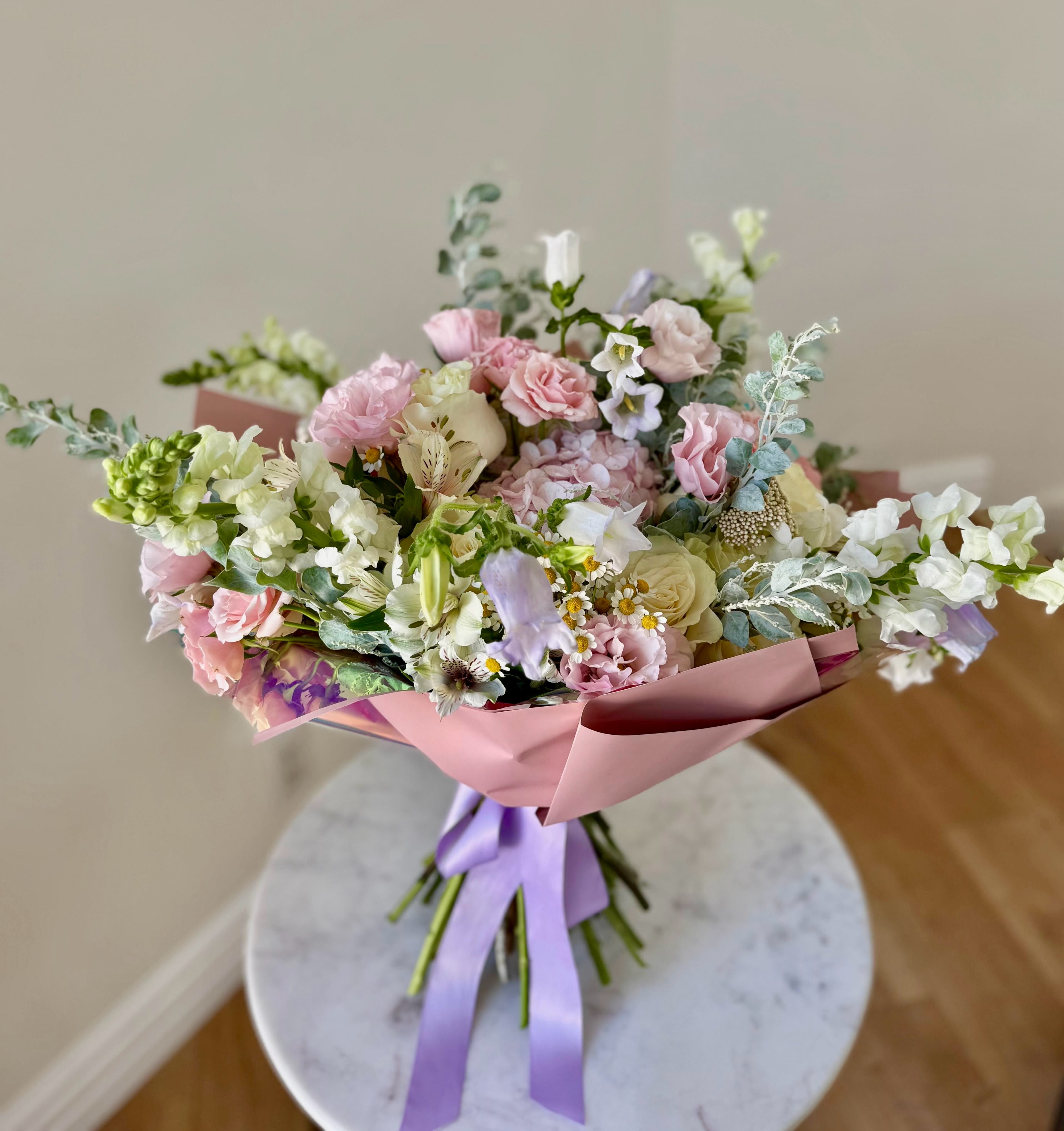 Pastel bouquet of pink, white, and lavender flowers wrapped in pink paper