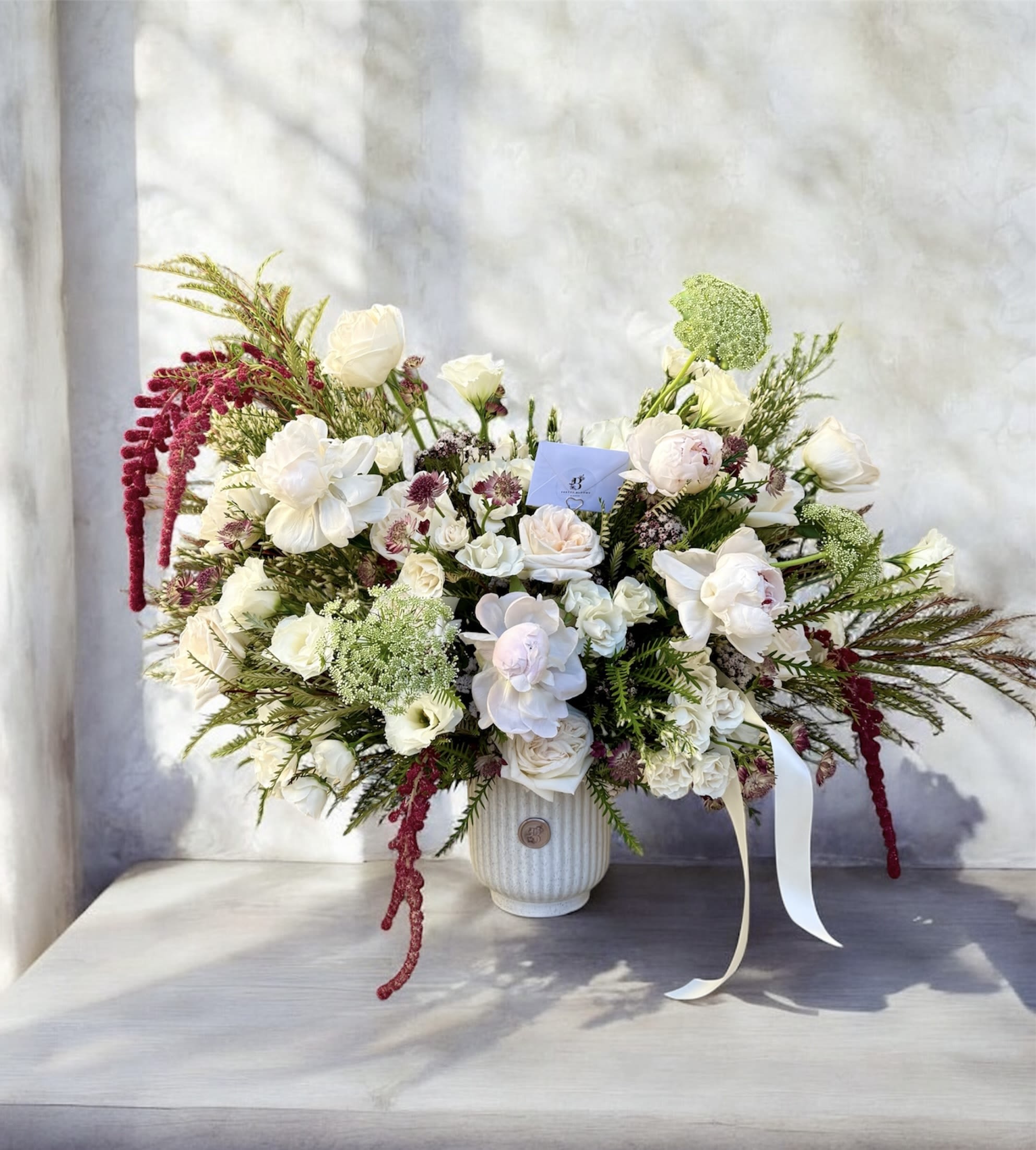 White and blush floral arrangement in a ribbed vase with trailing burgundy accents