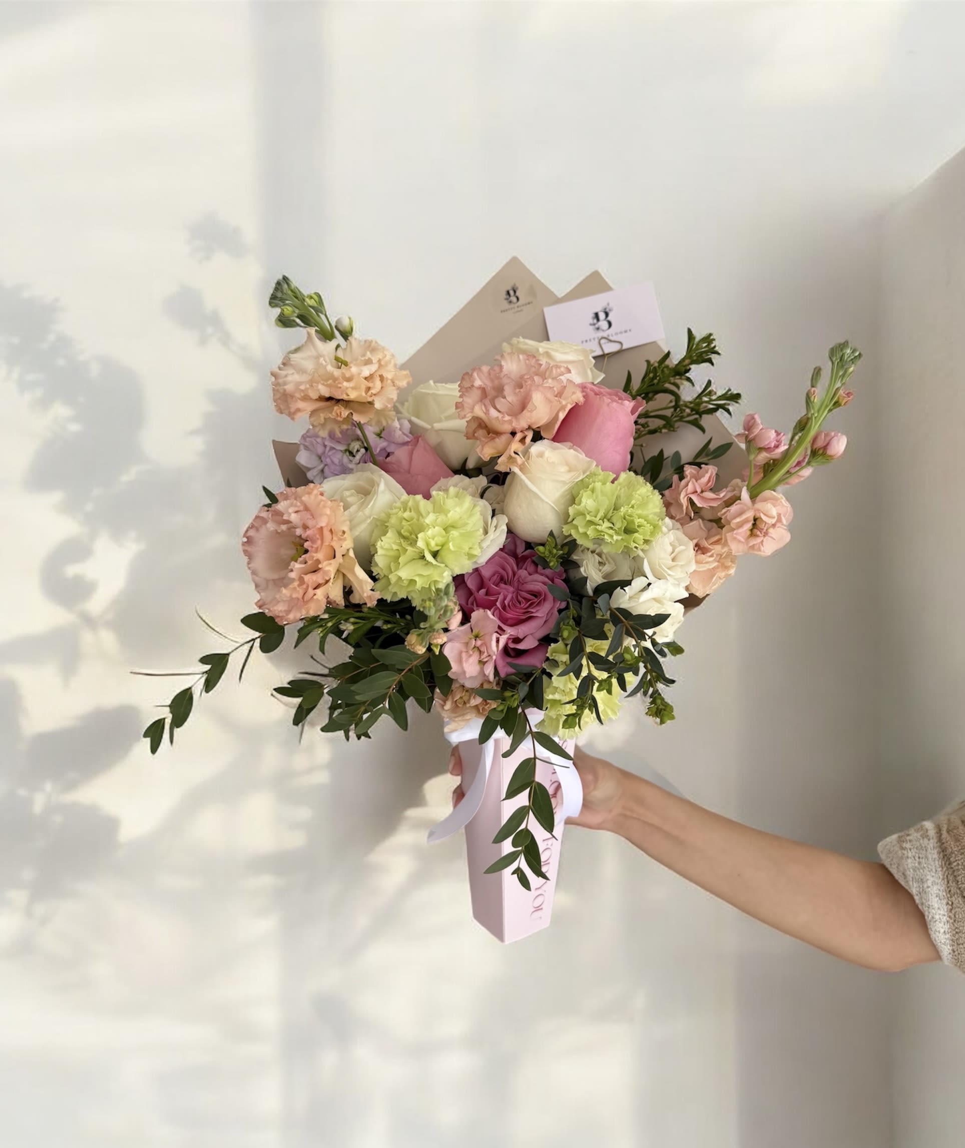 Handheld bouquet of pink, white, and peach flowers with greenery
