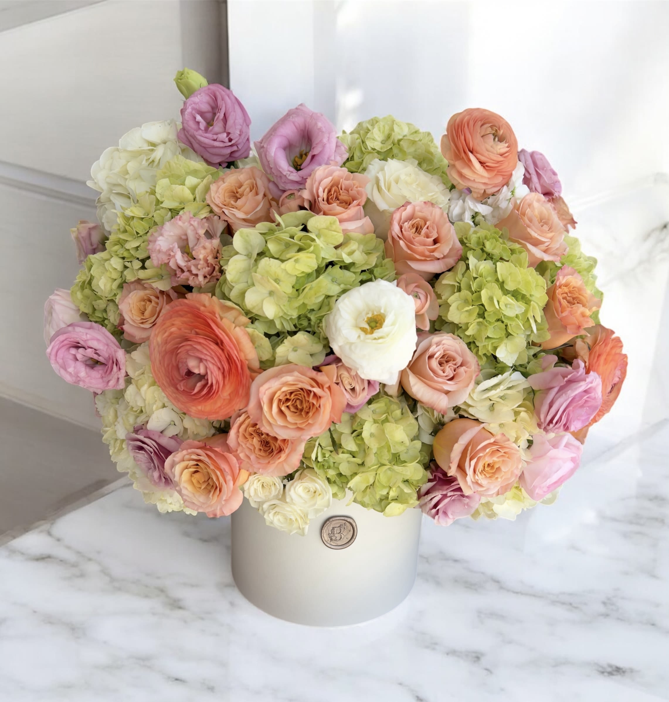 Pastel bouquet of roses, ranunculus, and hydrangeas in a white hat box
