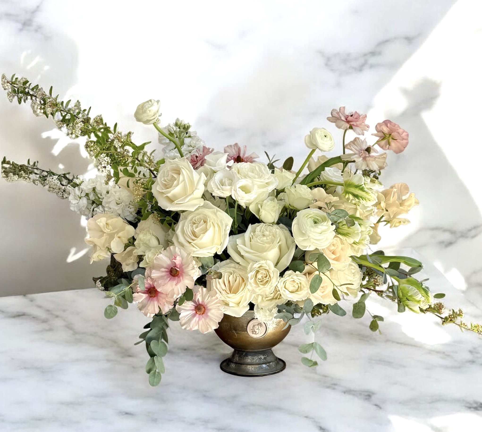 Cream and blush floral arrangement in a gold pedestal vase