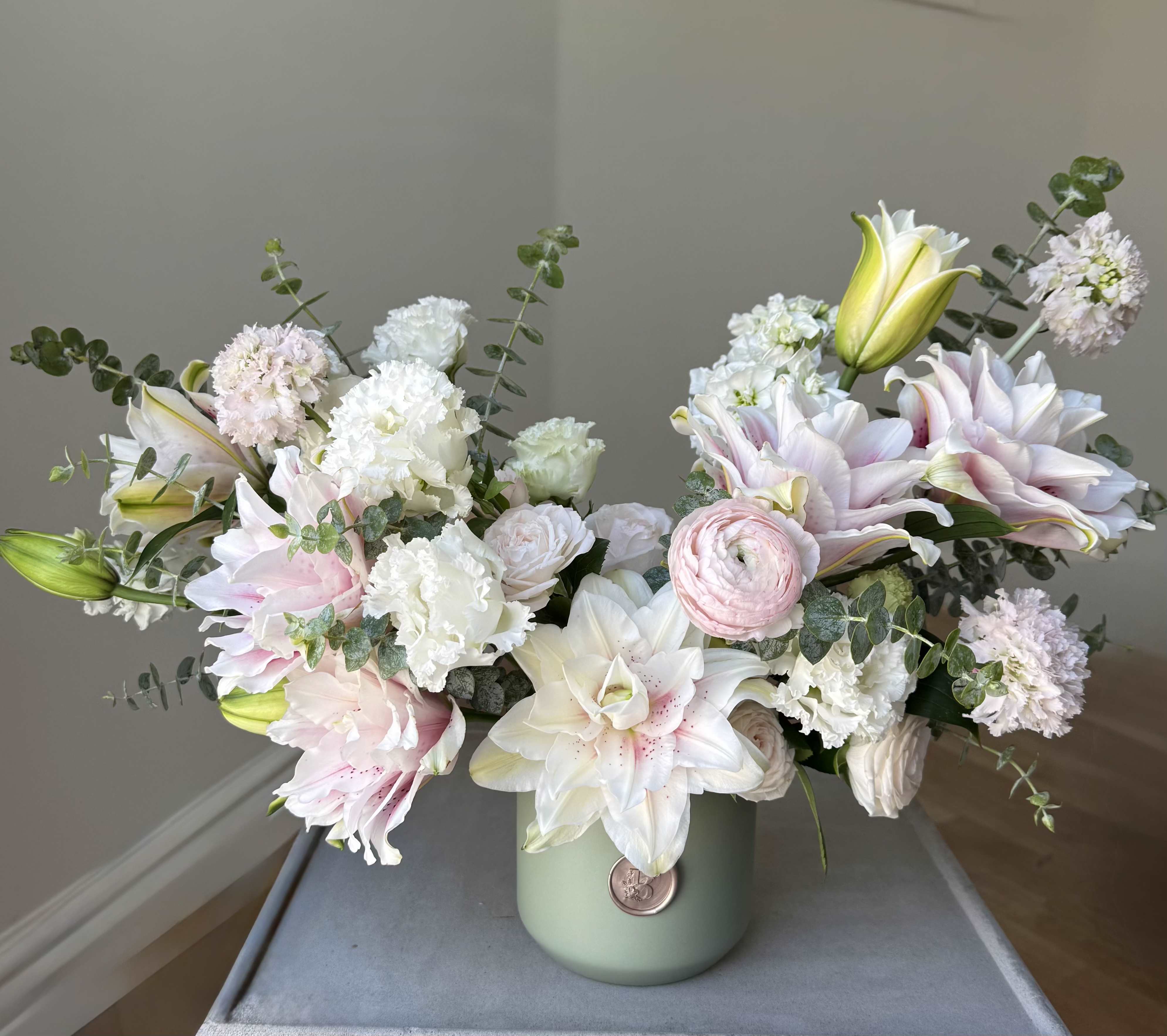 Pastel bouquet of lilies, carnations, and ranunculus in a green vase