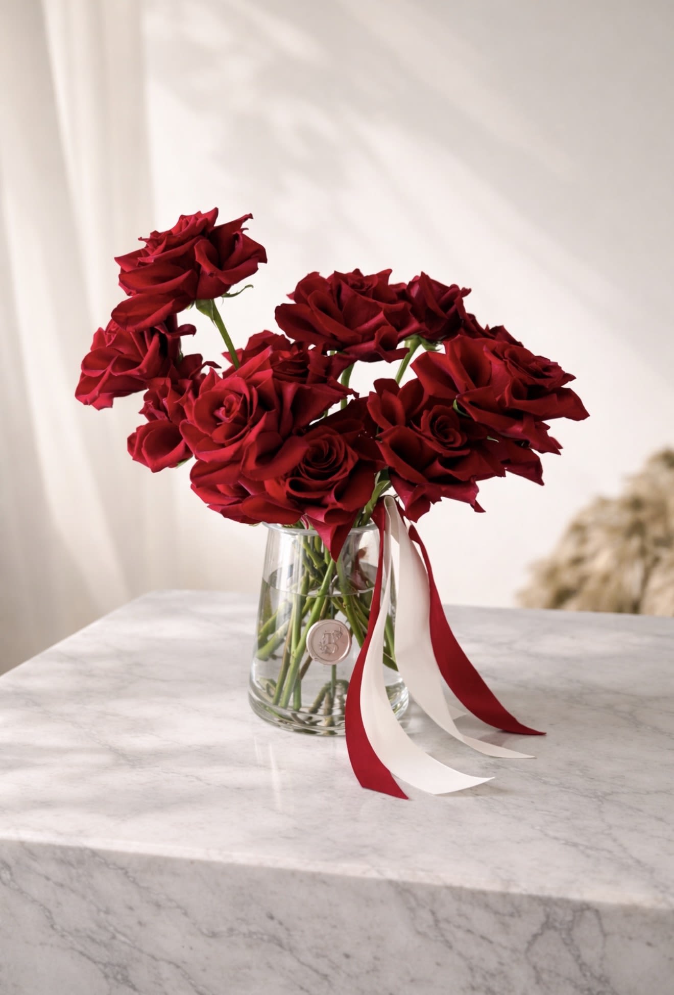 Red roses in a clear glass vase with red and white ribbons