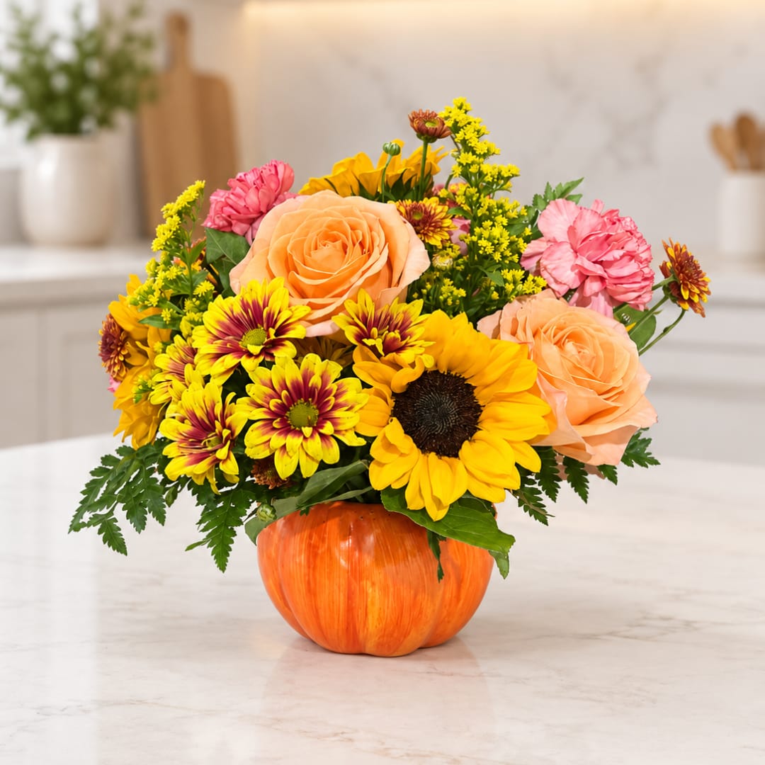 Bouquet of sunflowers, roses, and pink carnations in a pumpkin vase