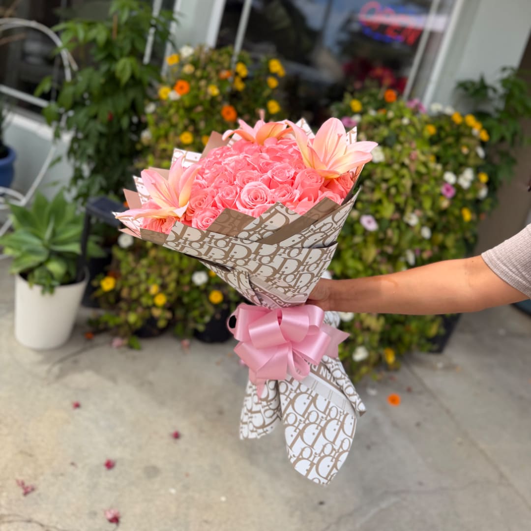 Pink rose bouquet with pale lilies wrapped in patterned paper and a pink bow