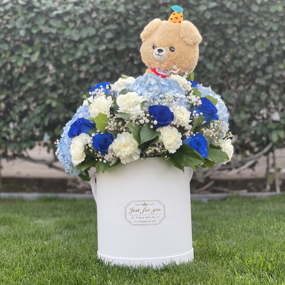 Blue and white flower arrangement in a white box with a teddy bear topper