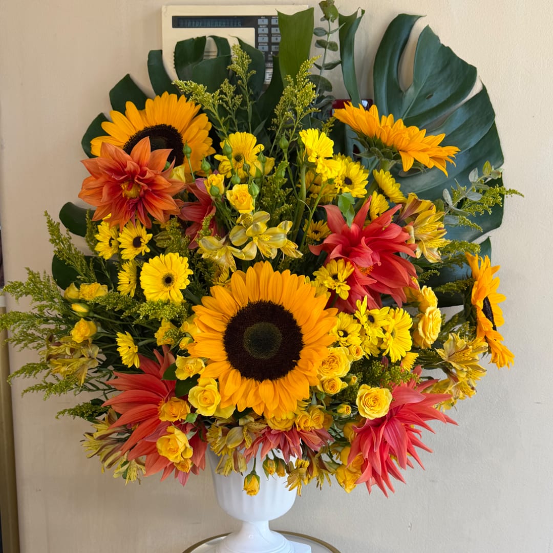 Bright mixed bouquet with sunflowers, yellow roses, and orange-red blooms in a white vase