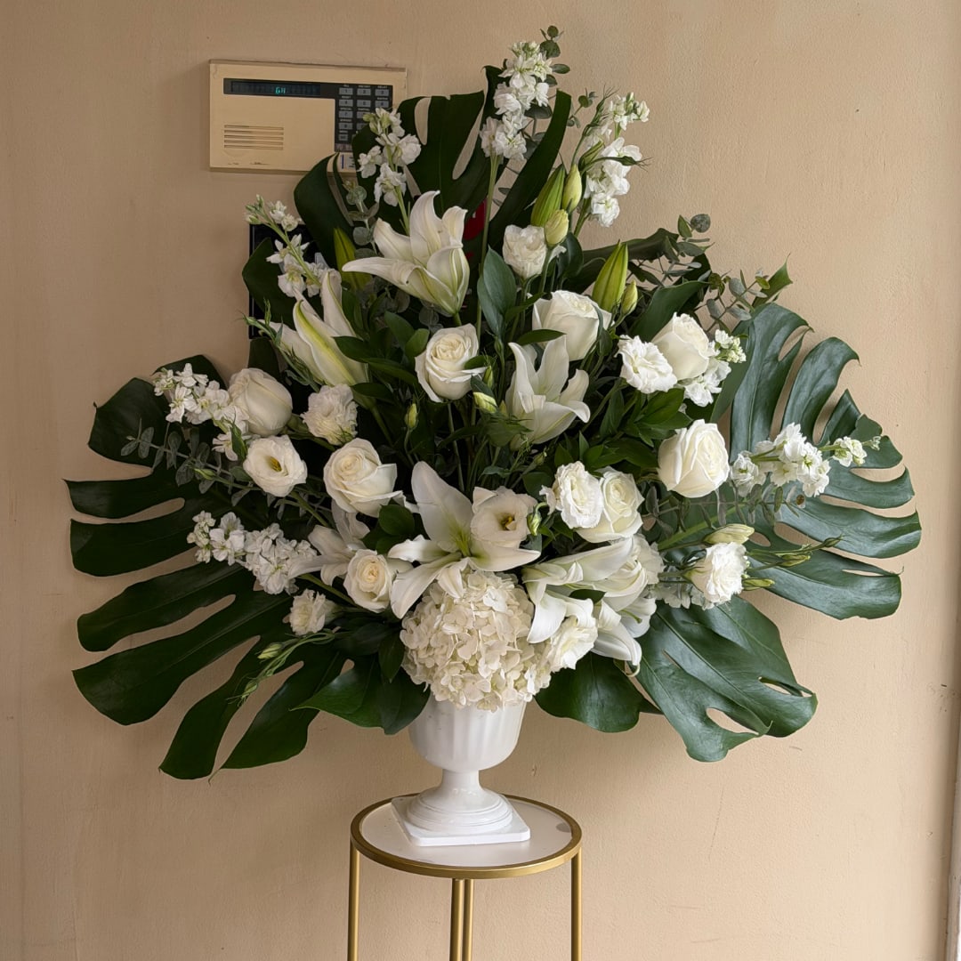White floral arrangement in a pedestal vase with large tropical leaves