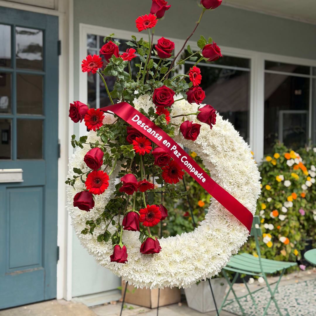 White floral wreath with red roses and gerbera daisies on a stand