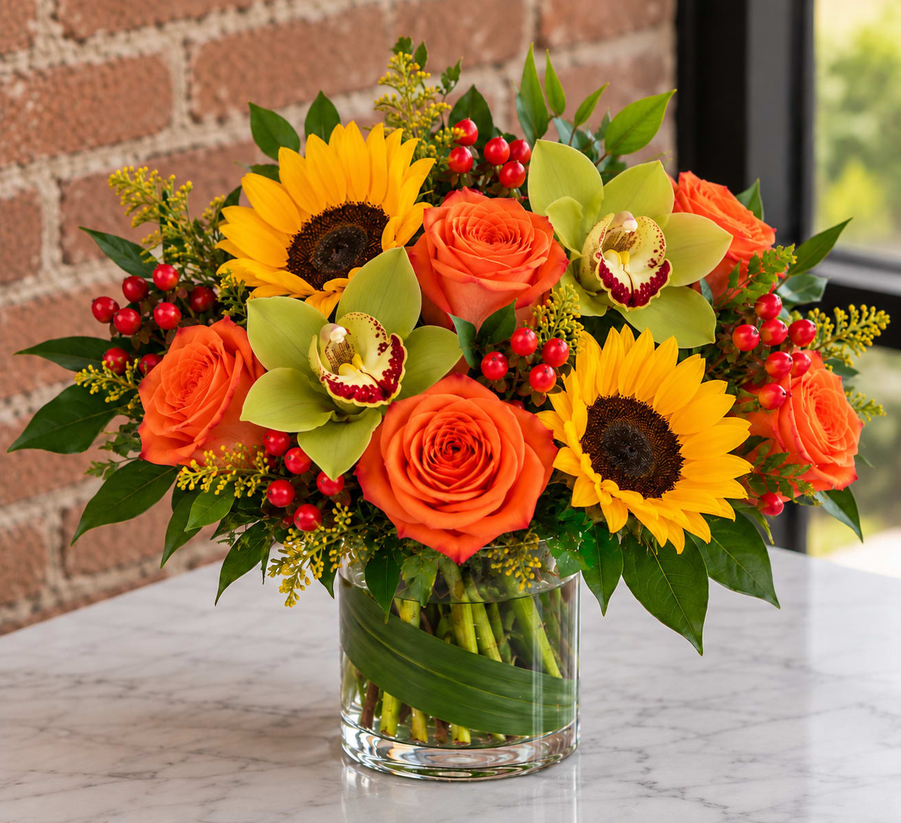 Orange roses and sunflowers in a glass vase with green orchids