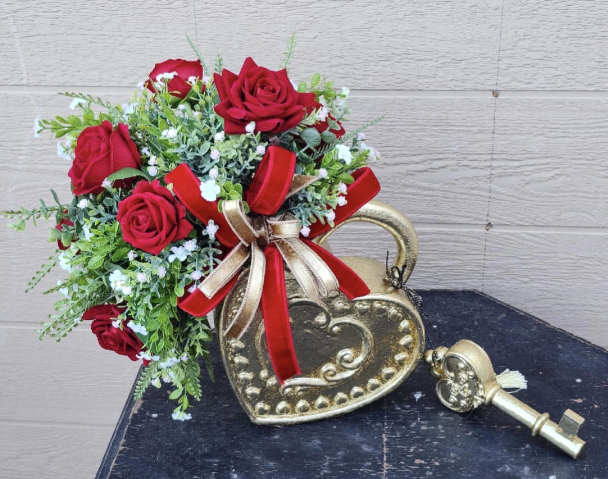 Red roses arranged in a gold heart-shaped container with ribbon.