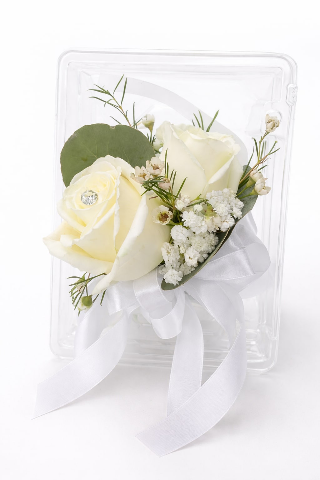     Classic White Rose Wrist Corsage - Ivory-white roses gathered into a wearable wrist corsage create a quietly elegant touch for weddings and other special occasions. This flower arrangement wrist corsage is designed as a delicate accessory-perfect for bridesmaids, mothers of the couple, or anyone who should feel honored-offering a soft, formal look that complements white or neutral attire.  Two ivory-white roses sit with tiny white filler blooms, a round green leaf, and slim greenery, all tied with a wide white ribbon and finished with a small decorative gem. The corsage is presented in a clear plastic box for safe transport and pristine presentation, emphasizing its compact, boutonniere-style scale and understated palette.  Give the person you're thinking of a classic, timeless accent that reads refined rather than fussy-ideal for weddings, proms, or formal events. The boxed presentation makes delivery and gifting simple; handle gently and keep cool until wear for best freshness.