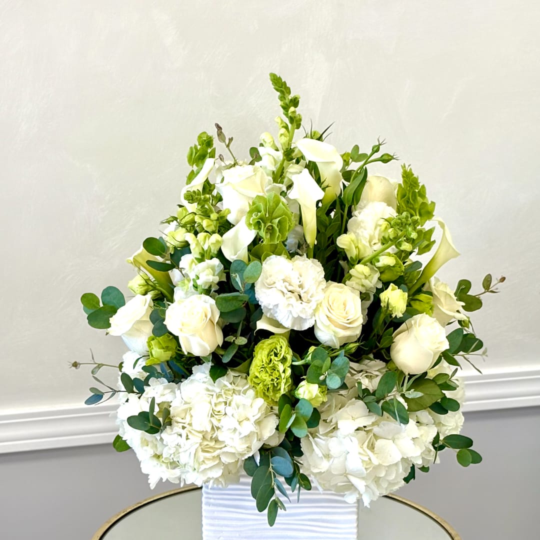 White floral arrangement in a ribbed white vase with green accents