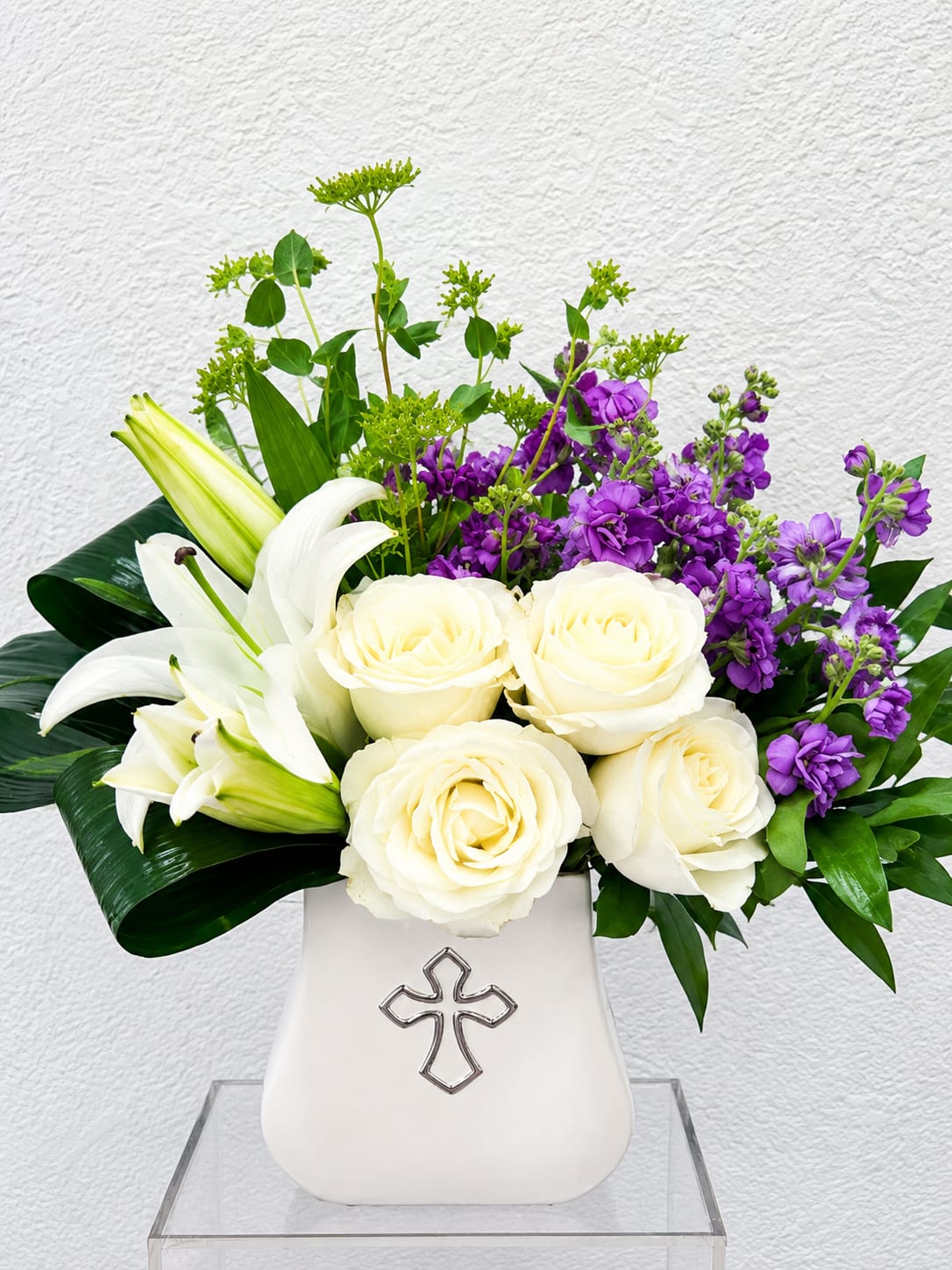 White roses and lilies arranged in a white vase with purple flowers