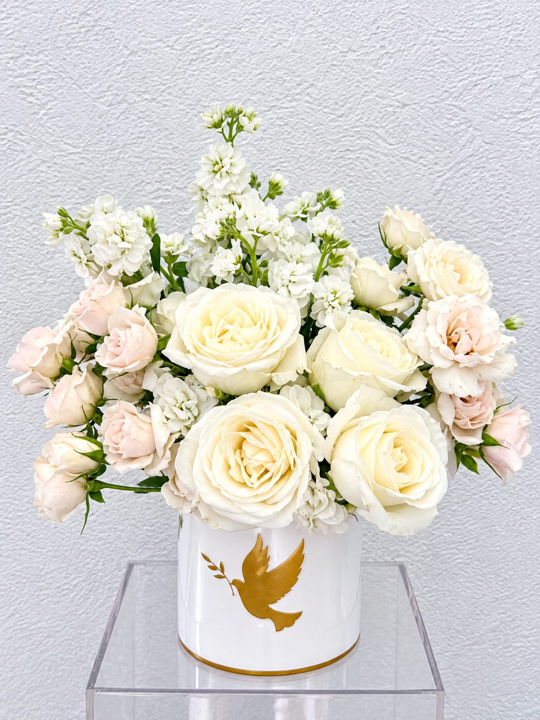 White and blush roses arranged in a white vase with a gold dove emblem