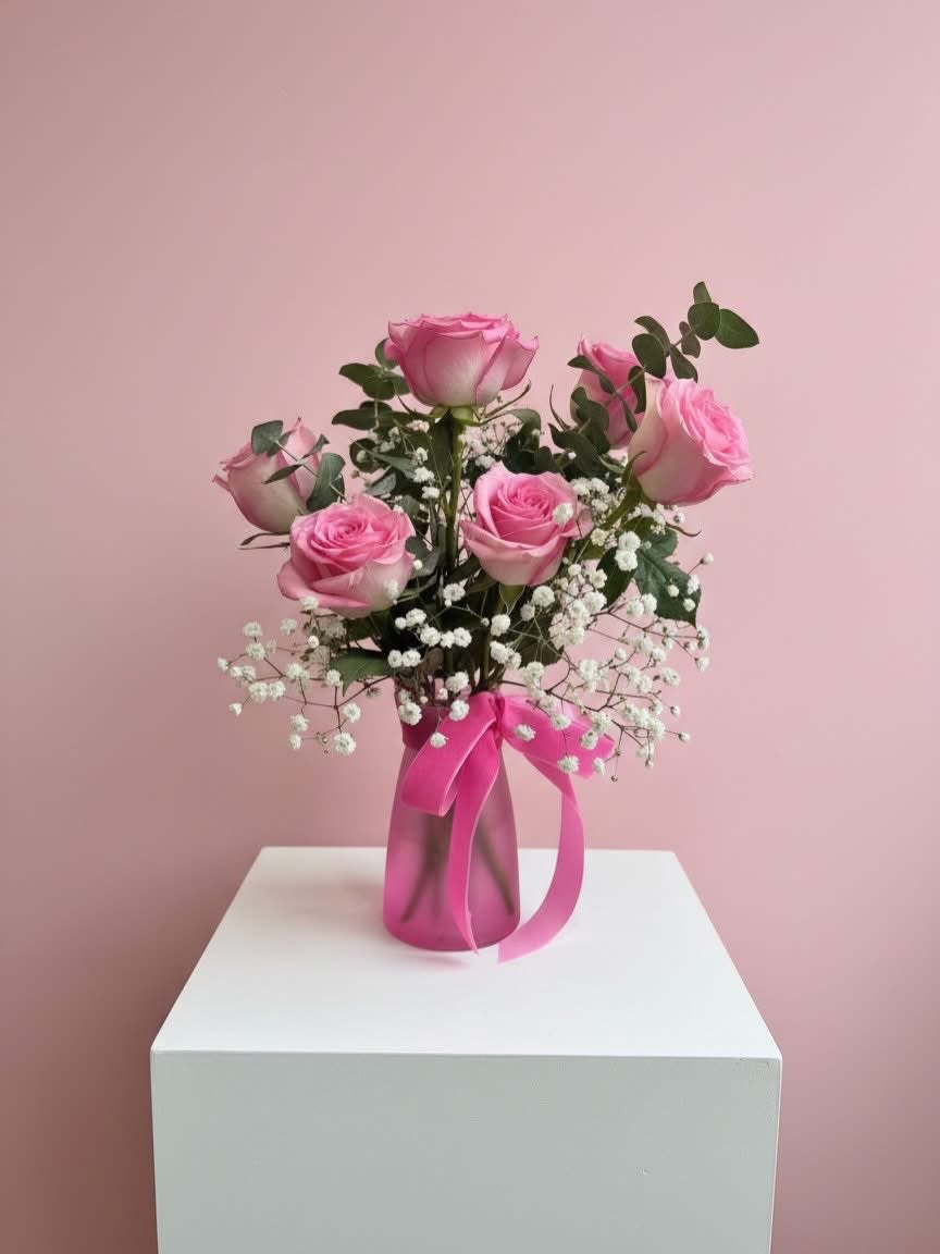 Pink roses arranged in a vase with baby's breath and a pink ribbon