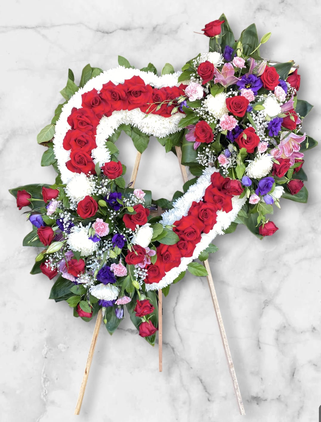 Large Sympathy Heart  - Beautifully crafted heart shape to honor the memory of a beloved individual. Created the base with, white chrysanthemums and adding red roses. With side bouquets of red roses adding purple lisianthus, star gazer lilies, carnation.