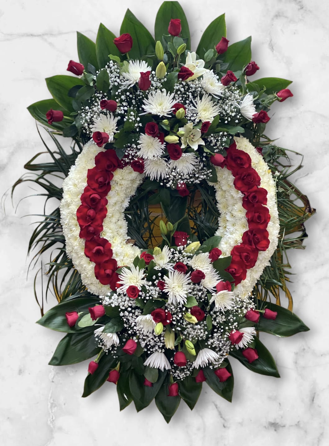 Large Sympathy Wreath  - Beautifully crafted wreath to honor the memory of a beloved individual. Created the base with, white chrysanthemums and adding red roses. With top and bottom bouquets of red roses adding spider mum and lilies.