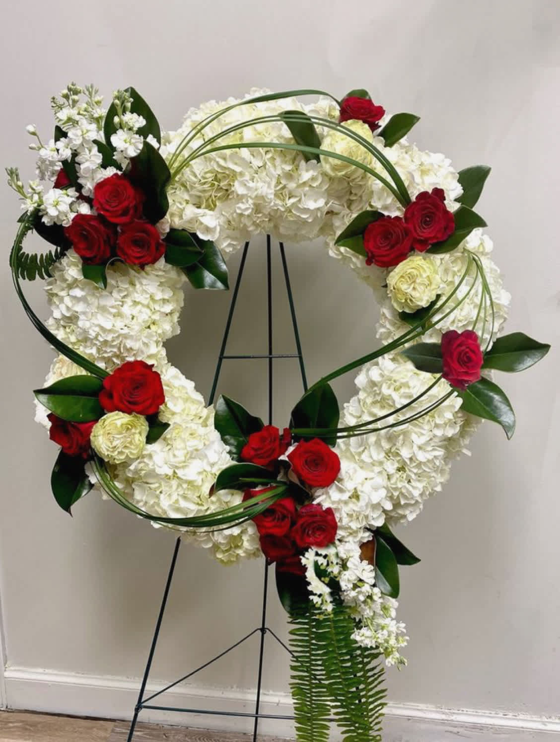 Heart-shaped floral wreath with red roses and white hydrangeas on a stand