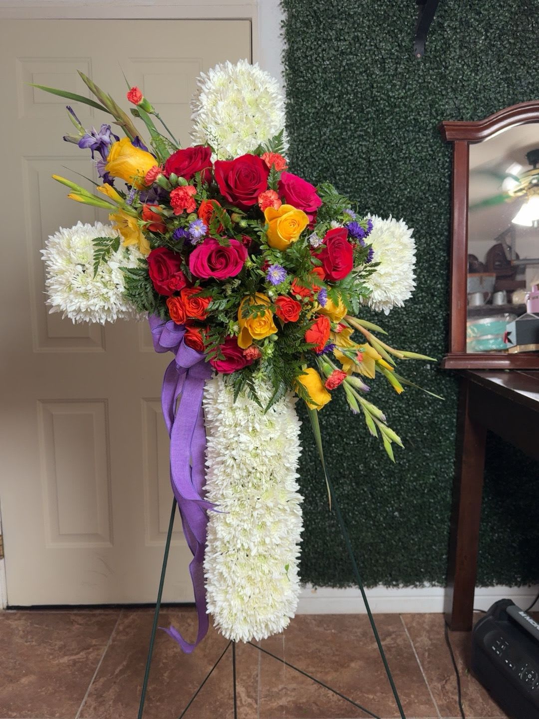 Standing floral cross with red, yellow, and white flowers on an easel