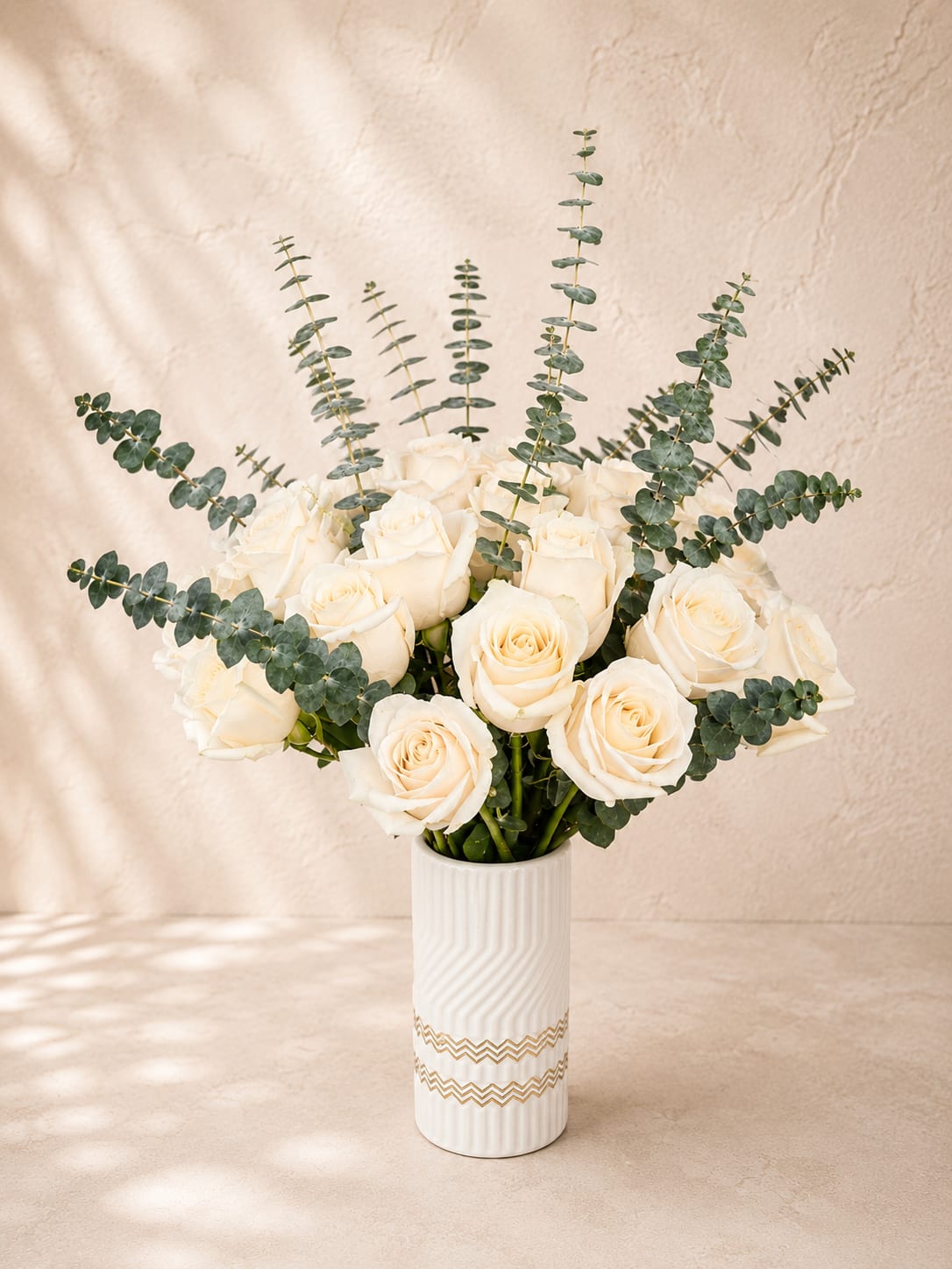 Aphrodite's Ivory Embrace - Graceful, refined, and effortlessly elegant, Aphrodite's Ivory Embrace showcases 24 premium white roses arranged with fresh silver dollar eucalyptus in a modern ceramic vase. The crisp white blooms symbolize purity, sincerity, and everlasting love, while the airy eucalyptus adds natural texture and a contemporary garden feel.  Perfect for anniversaries, weddings, sympathy, birthdays, congratulations, or simply expressing heartfelt appreciation, this timeless arrangement complements any home or office with understated luxury.  Each arrangement is handcrafted by Flower Fairy using the freshest premium roses available. Minor substitutions in greenery or vase may occasionally be necessary while preserving the overall style and value.  Features: 24 premium white roses Fresh silver dollar eucalyptus Premium white ceramic vase Elegant modern design Handcrafted by Flower Fairy Same-day delivery throughout the Phoenix Metro Area