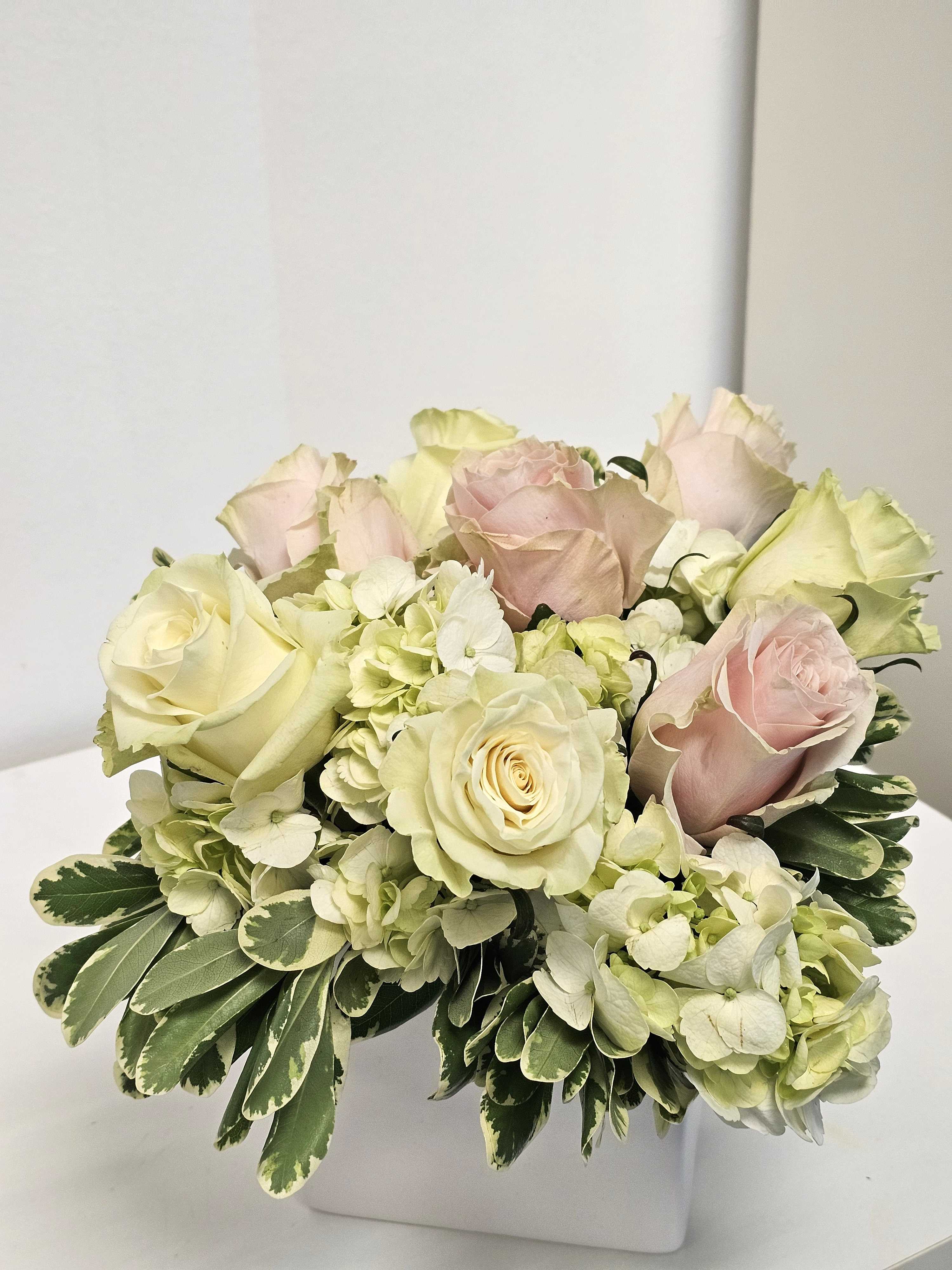 Arrangement of pale roses and hydrangeas in a white square vase