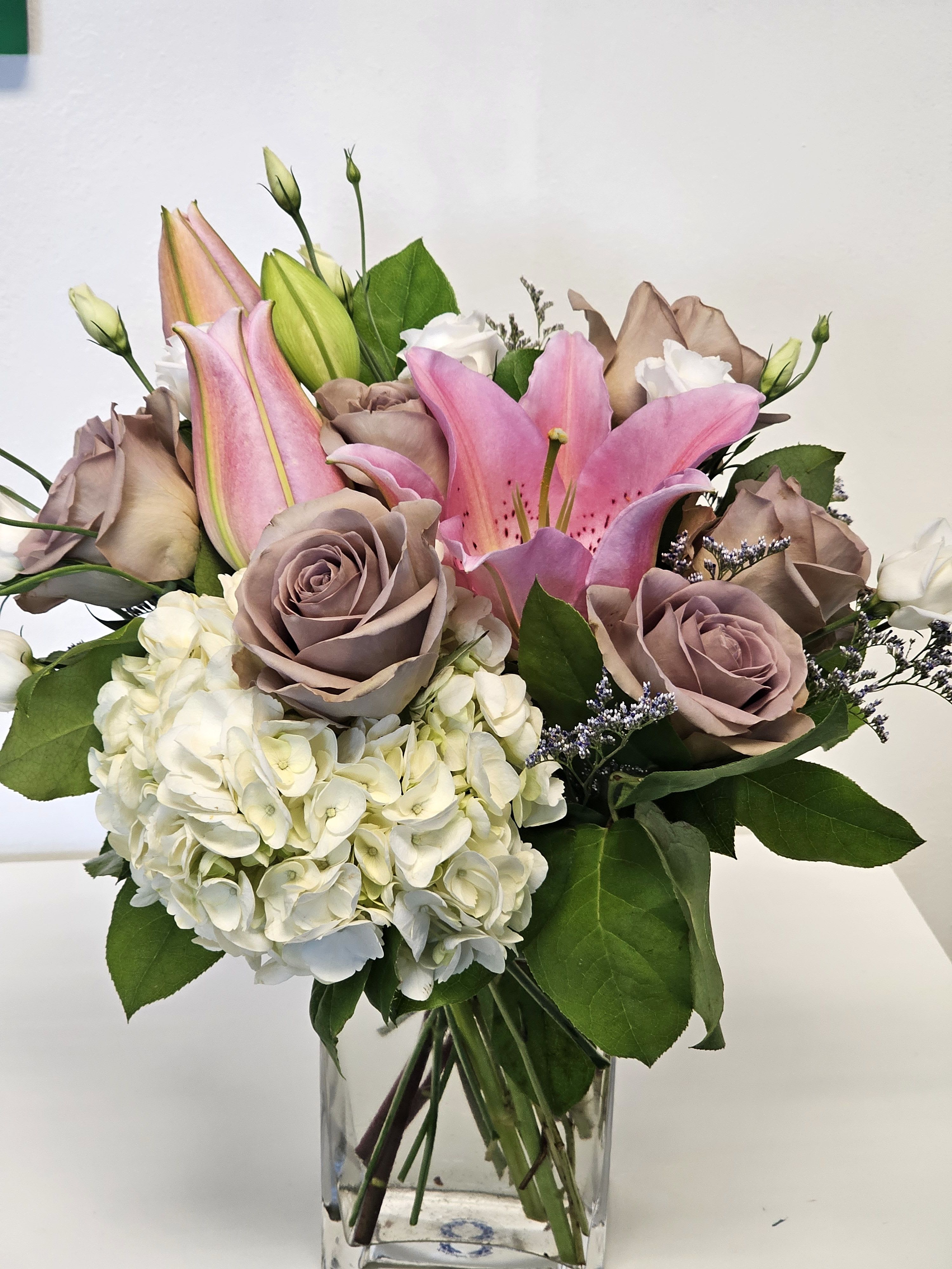 Beautifull arrangement with purple roses. -  floral arrangement, where the star of the show is the captivating purple rose. These luxurious roses, symbolizing enchantment and love at first sight, are surrounded by complementary blooms such as lavender-hued lisianthus, deep purple orchids, and soft white baby's breath. The combination creates a harmonious blend of color and texture. Accents of rich green foliage, like ruscus or ivy, provide a striking contrast, making the purple tones pop even more. Arranged in a modern, clear glass vase or a rustic wicker basket, this arrangement is a perfect choice for expressing admiration, celebrating a milestone, or simply bringing a touch of magic to any space.