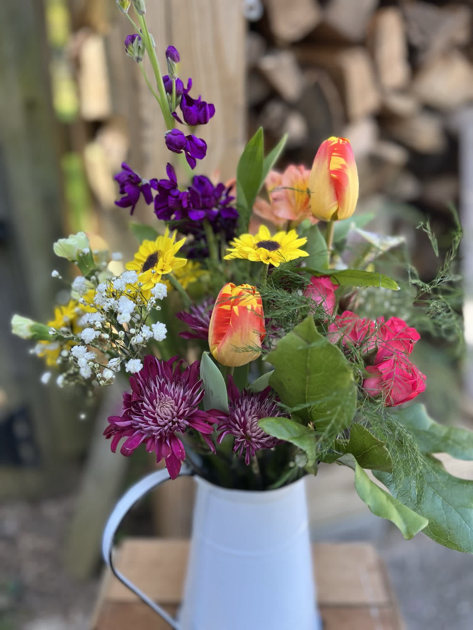 Mixed bouquet with purple, yellow, and pink flowers in a white pitcher vase
