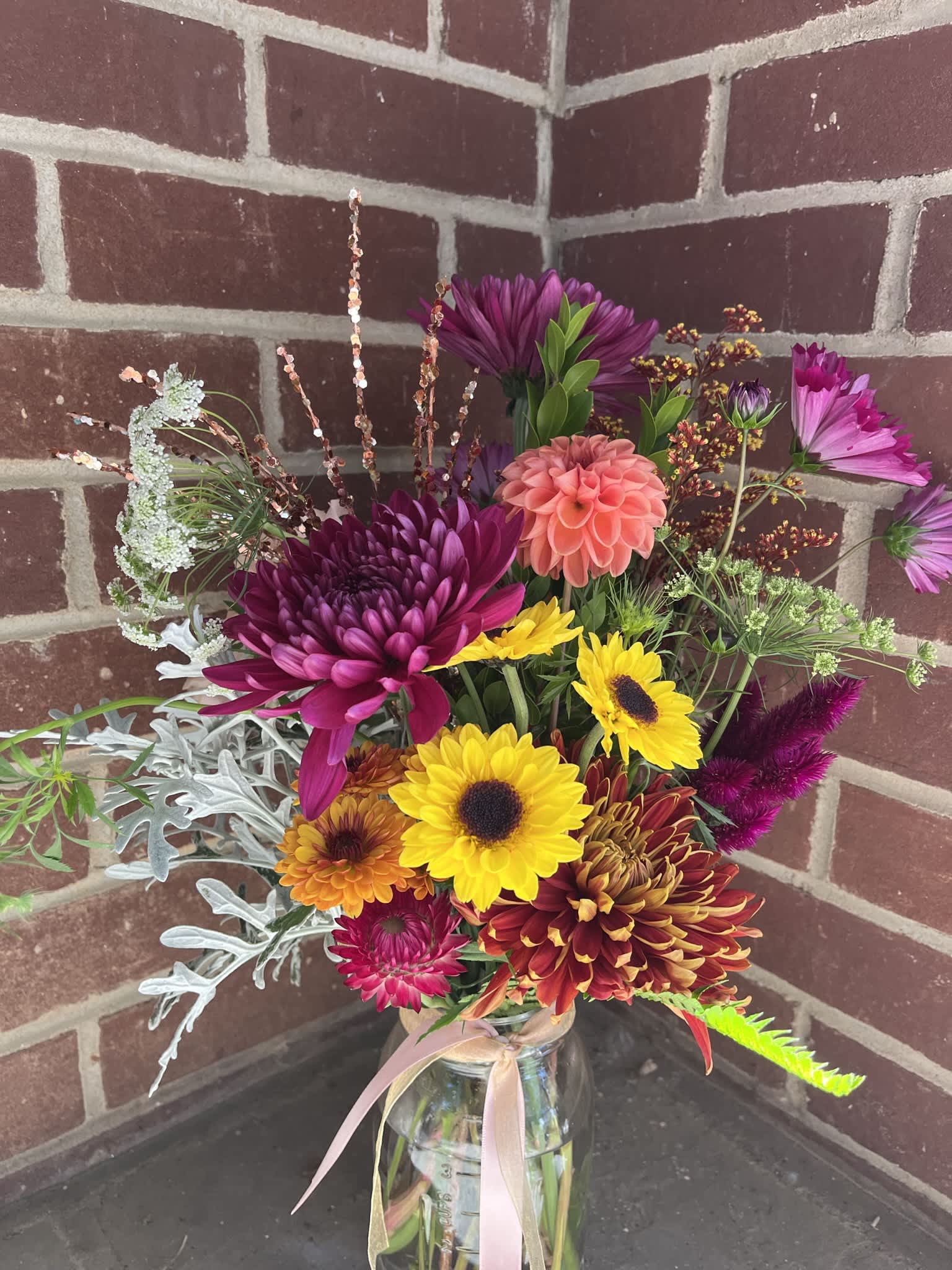 Mixed bouquet of bright chrysanthemums and sunflowers in a glass jar vase