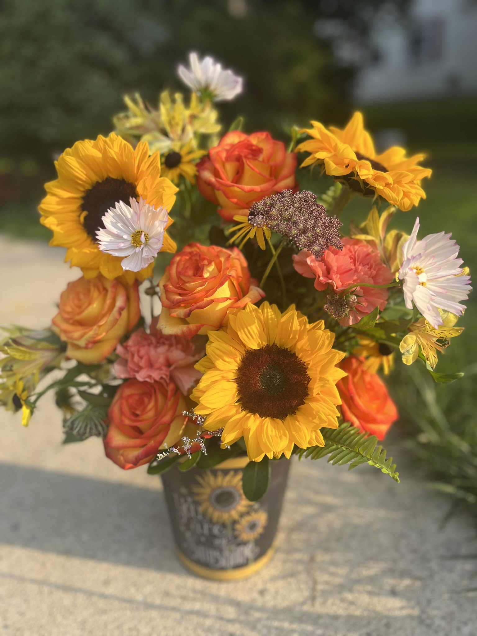 You Are My Sunshine - A fall arrangement bursting with sunflowers and roses interspersed with other locally available flowers such as celosia, lisanthus, rudbeckia, cosmos, gomphrena, and strawflowers in a metal pail with "You Are My Sunshine."  