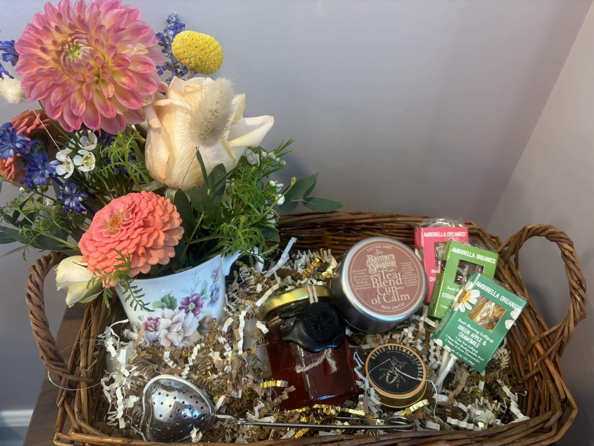 Cup of Calm Basket - A basket filled with flowers, tea, and treats.  The flower arrangement comes in an upcycled teacup using stunning fresh cut flowers.  The basket has a tin of "Cup of Calm," a tea created by a local tea shop called The Reister's Daughter.  Then a 4oz. container of Hexed honey from a local Baltimore apiary, Bees Wax Lip Balm, and an adorable heart shaped tea infuser.    Cup of Calm tea contains: Chamomile, lavender, stevia leaf, rose petals, skullcap, lemon balm, and red clover for a relaxing blend.  The tea is non-caffeinated.   