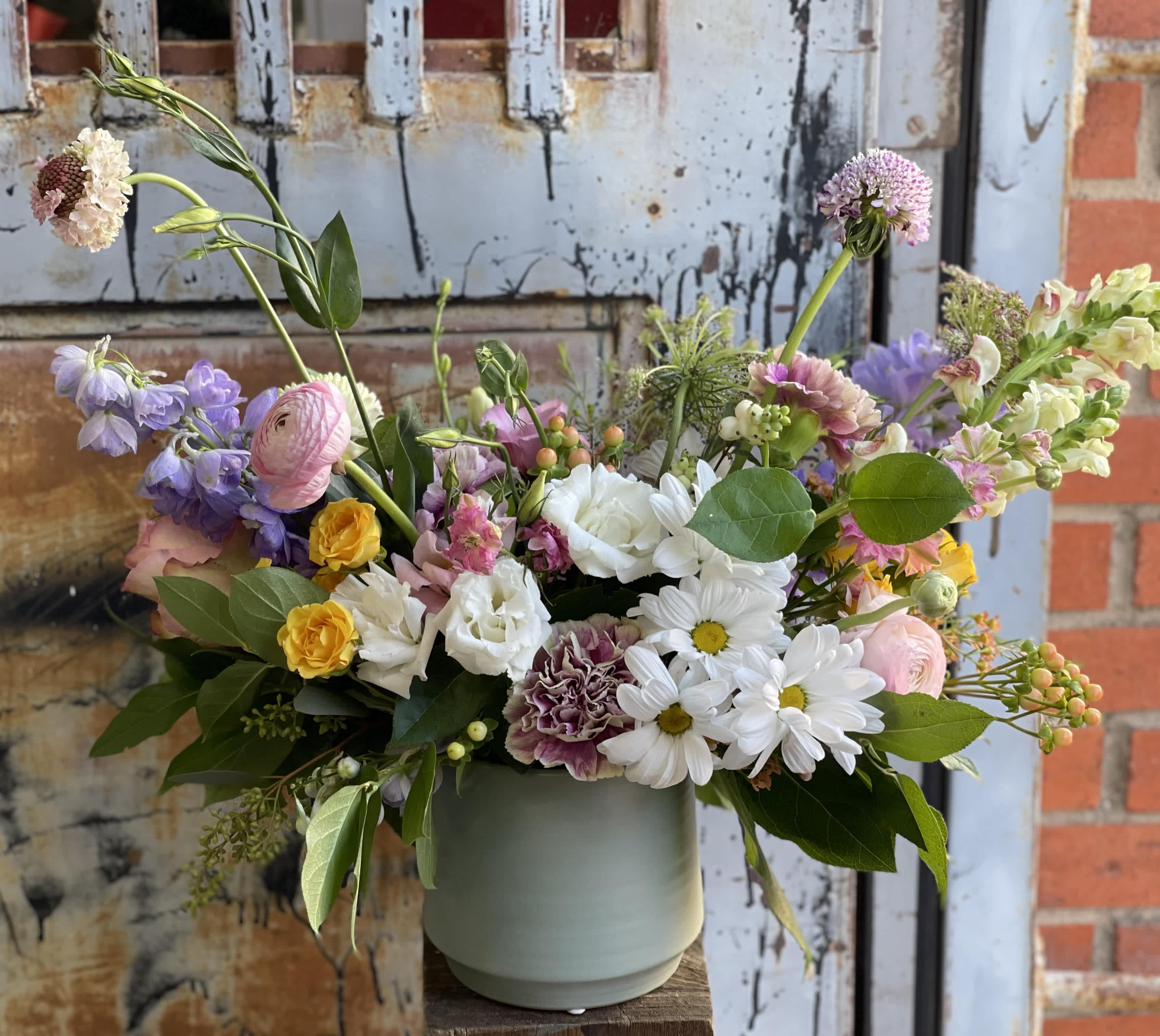 Mixed bouquet in a pale green vase with white, pink, purple, and yellow flowers