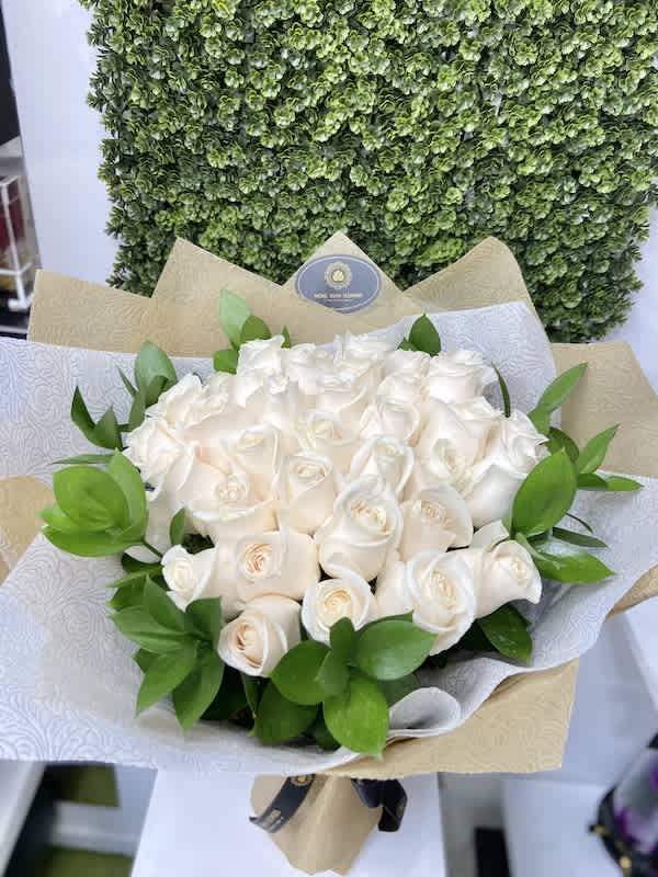 Bouquet of cream-colored roses wrapped in patterned white and kraft paper with a bow.