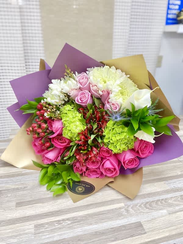 Hand-tied bouquet with pink roses, green hydrangeas, white chrysanthemums and red blooms in purple and gold wrap