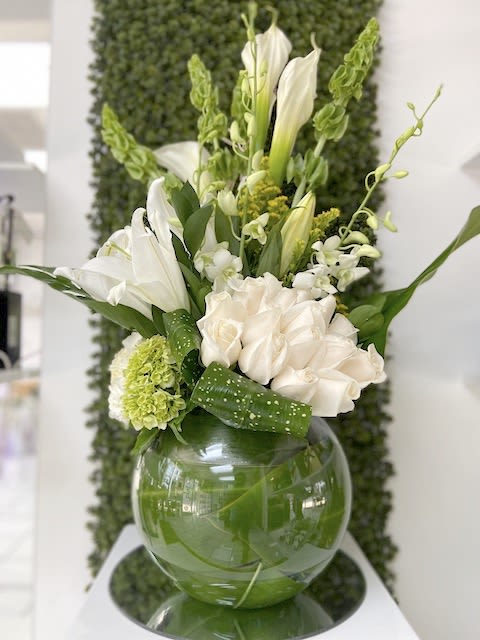 White and green flower arrangement with calla lilies and roses in a round glass vase