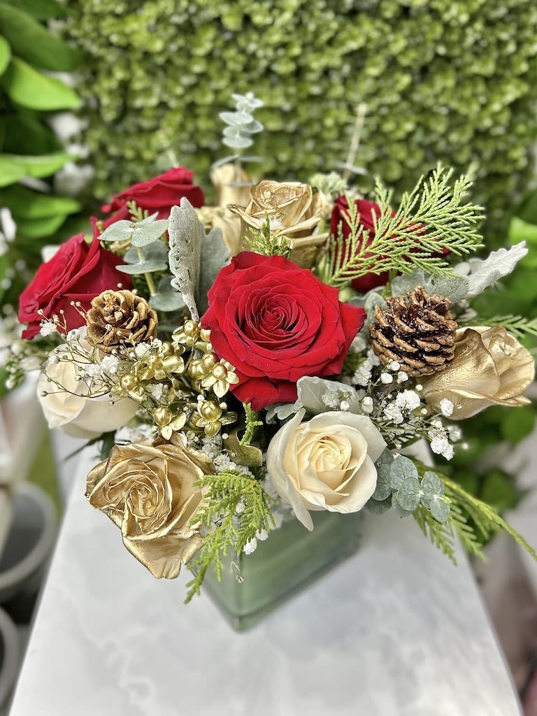Red, white, and gold roses with pinecones in a green glass cube vase