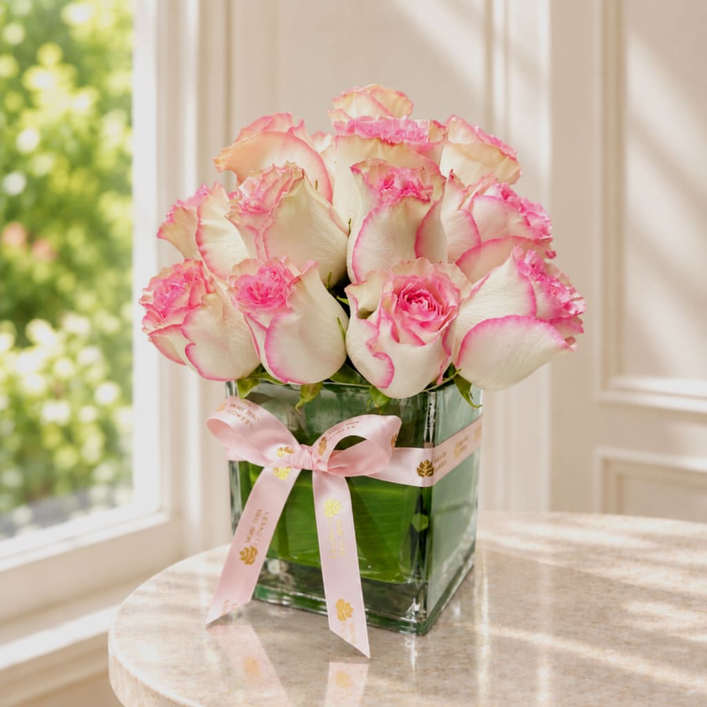 Pink-edged white roses in a square glass vase with a pink ribbon