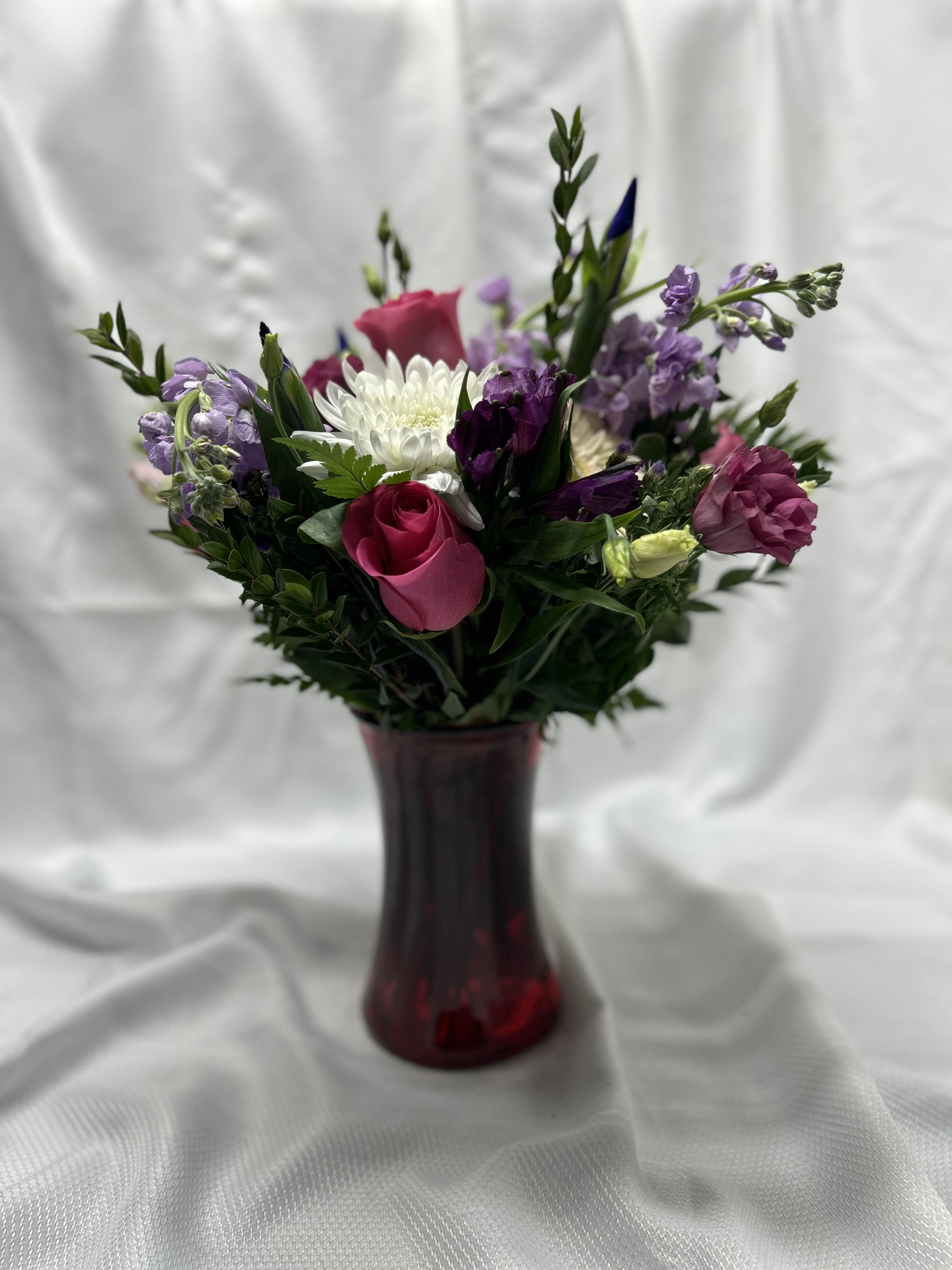 Mixed bouquet of pink, white, and purple flowers in a red vase