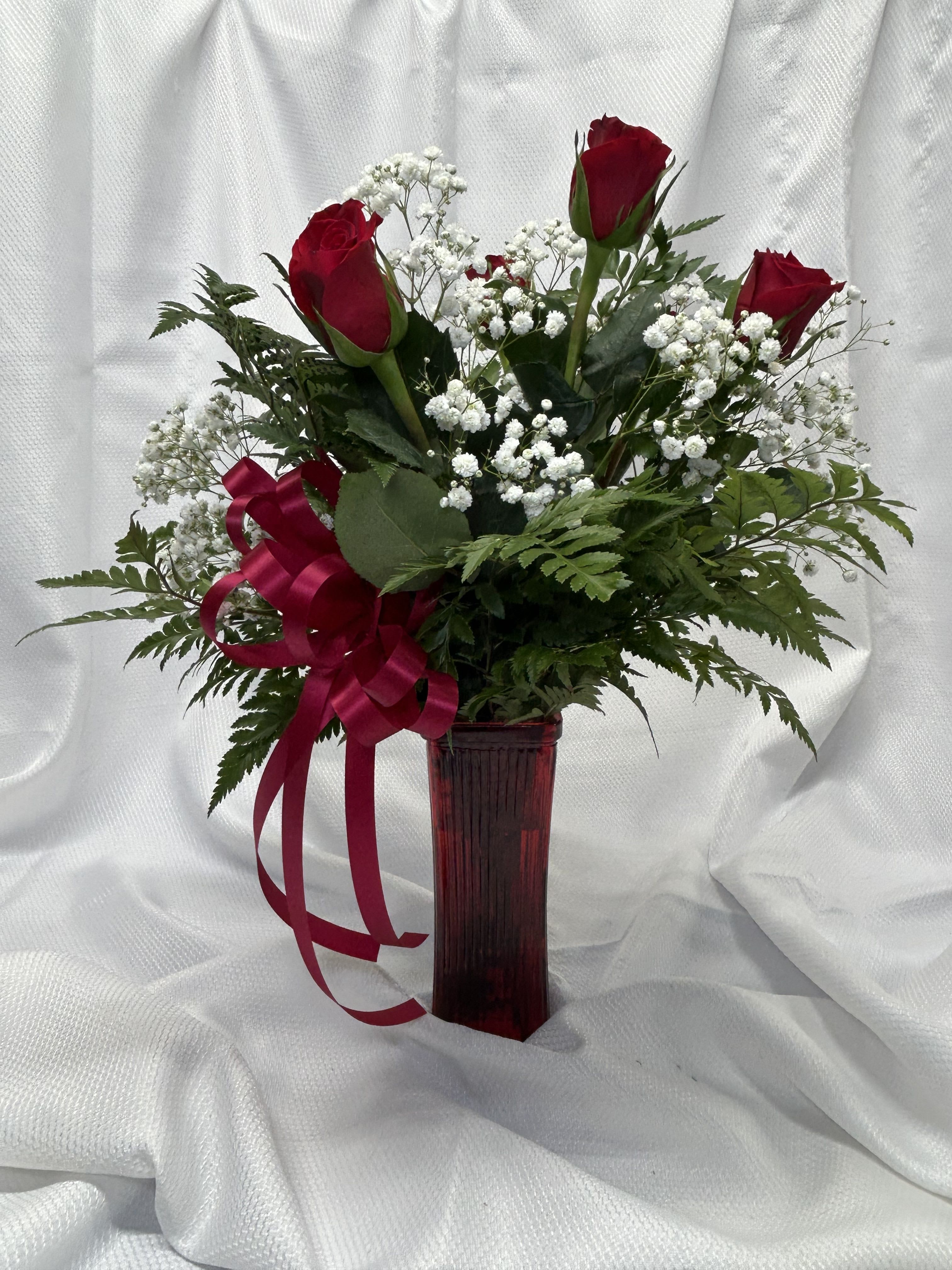 Red roses with baby's breath in a tall red vase with ribbon