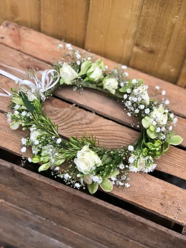 White floral wreath with small blossoms and ribbon on a wooden surface
