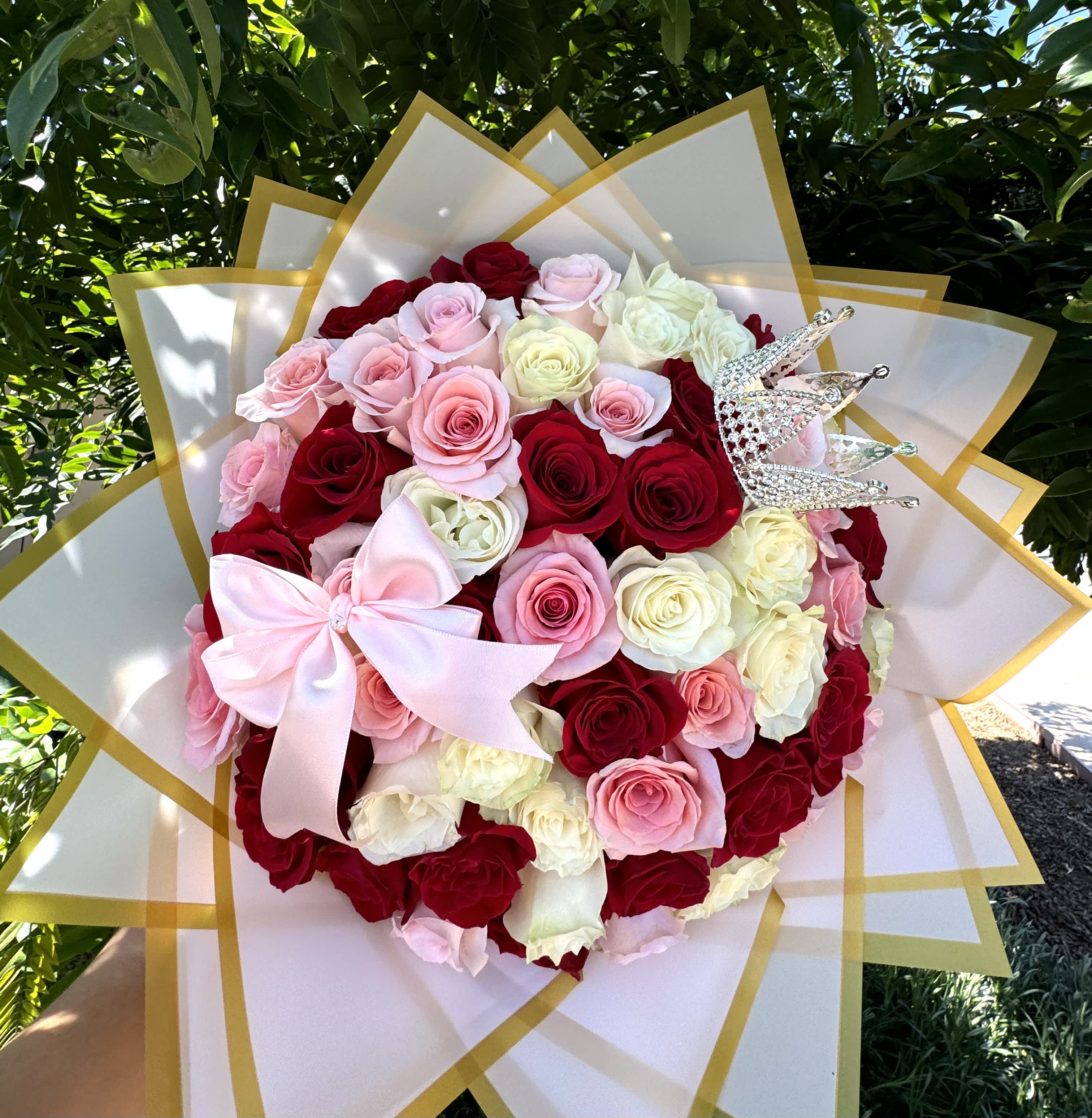 Round bouquet of red, pink, and white roses with a pink bow and crown pick