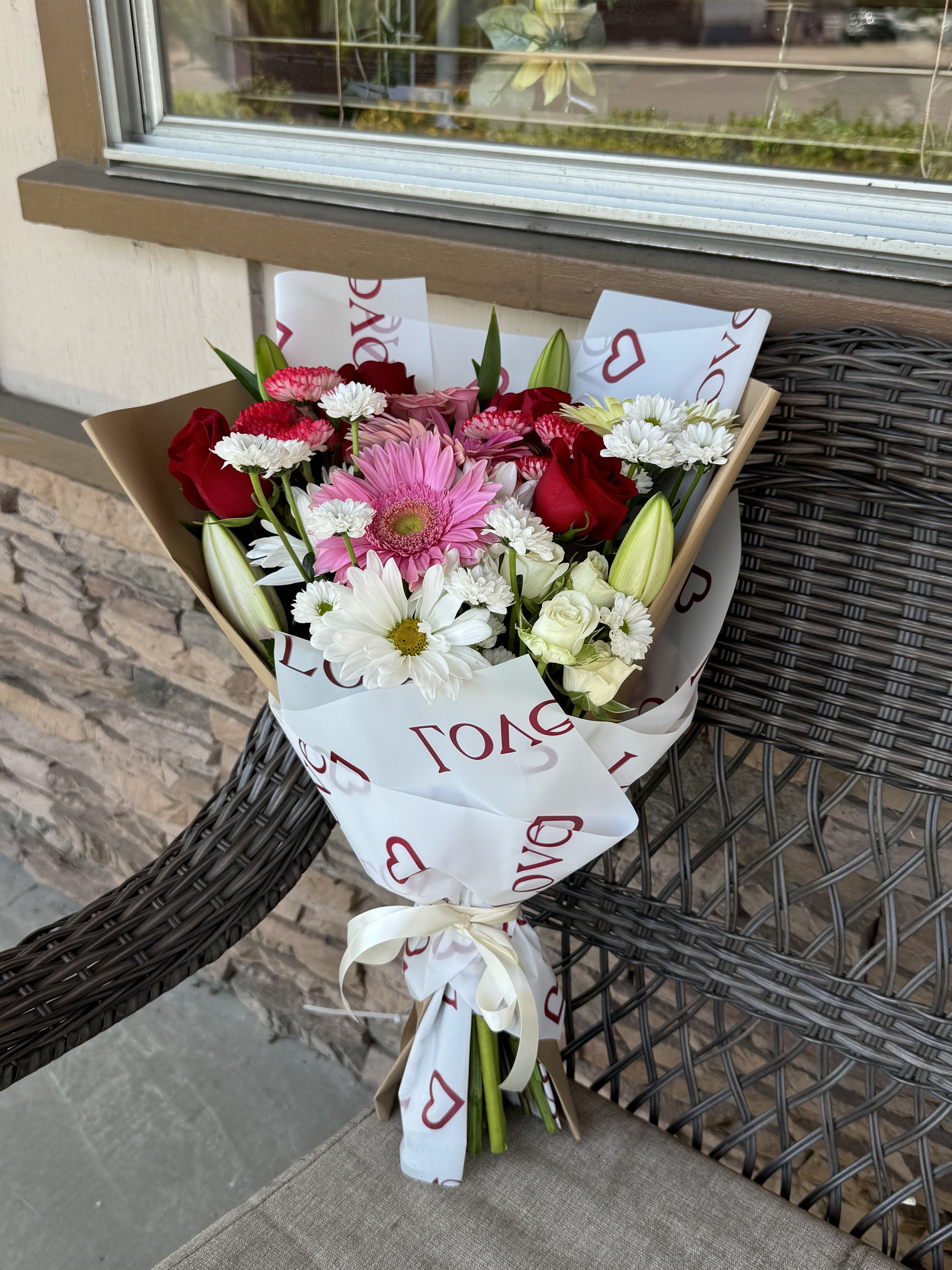 Bouquet of pink, red, and white flowers wrapped in paper with a ribbon