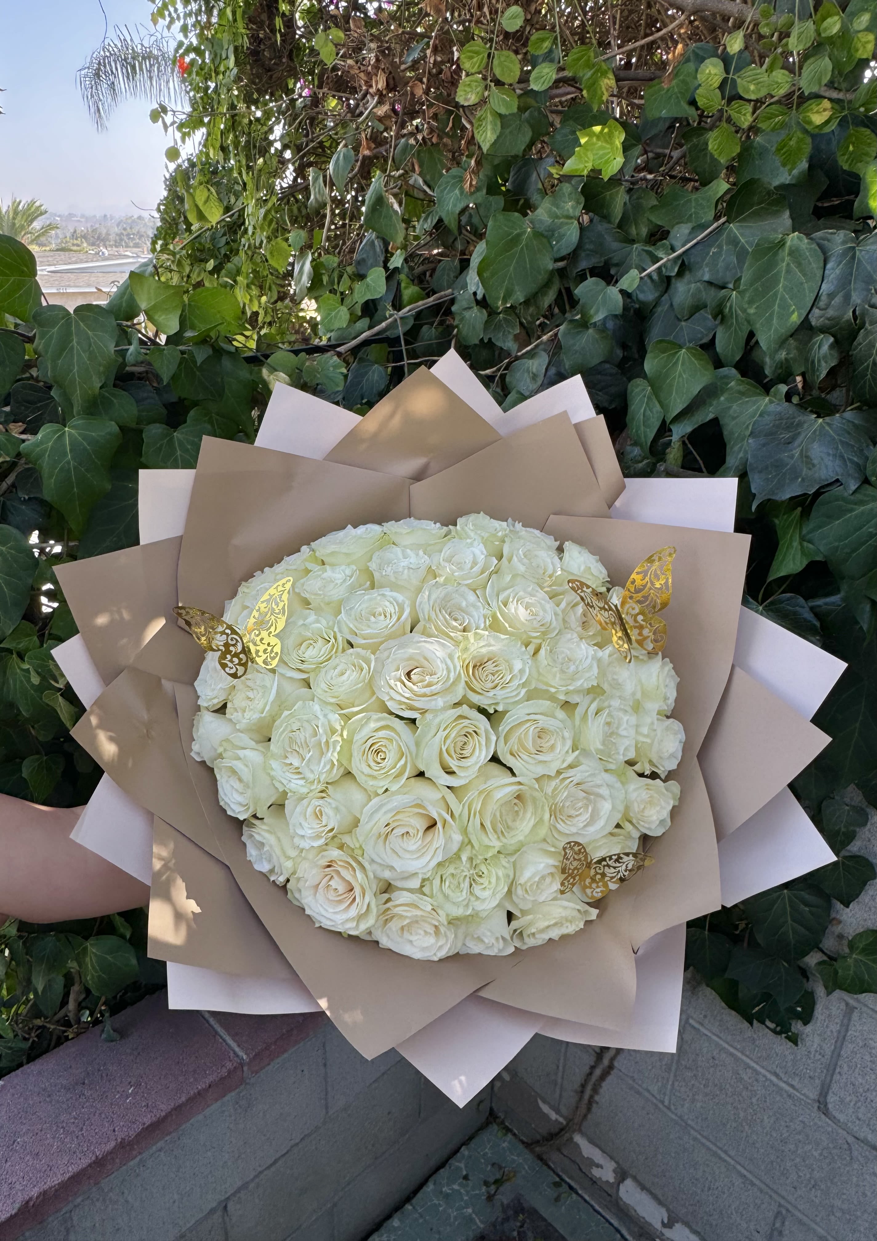 Bouquet of white roses wrapped in tan paper with gold butterfly accents