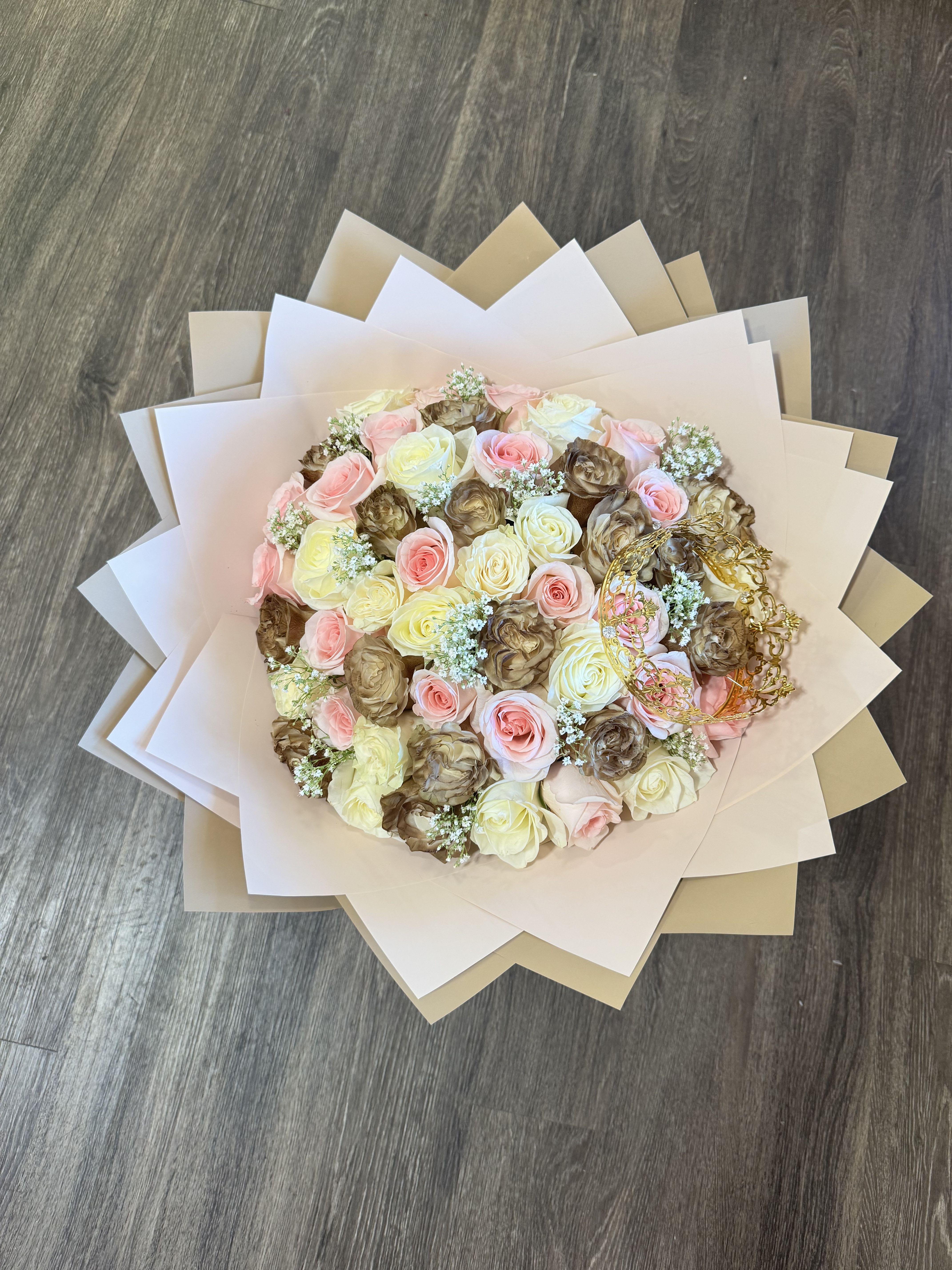 Round bouquet of pink, cream, and brown roses wrapped in layered paper