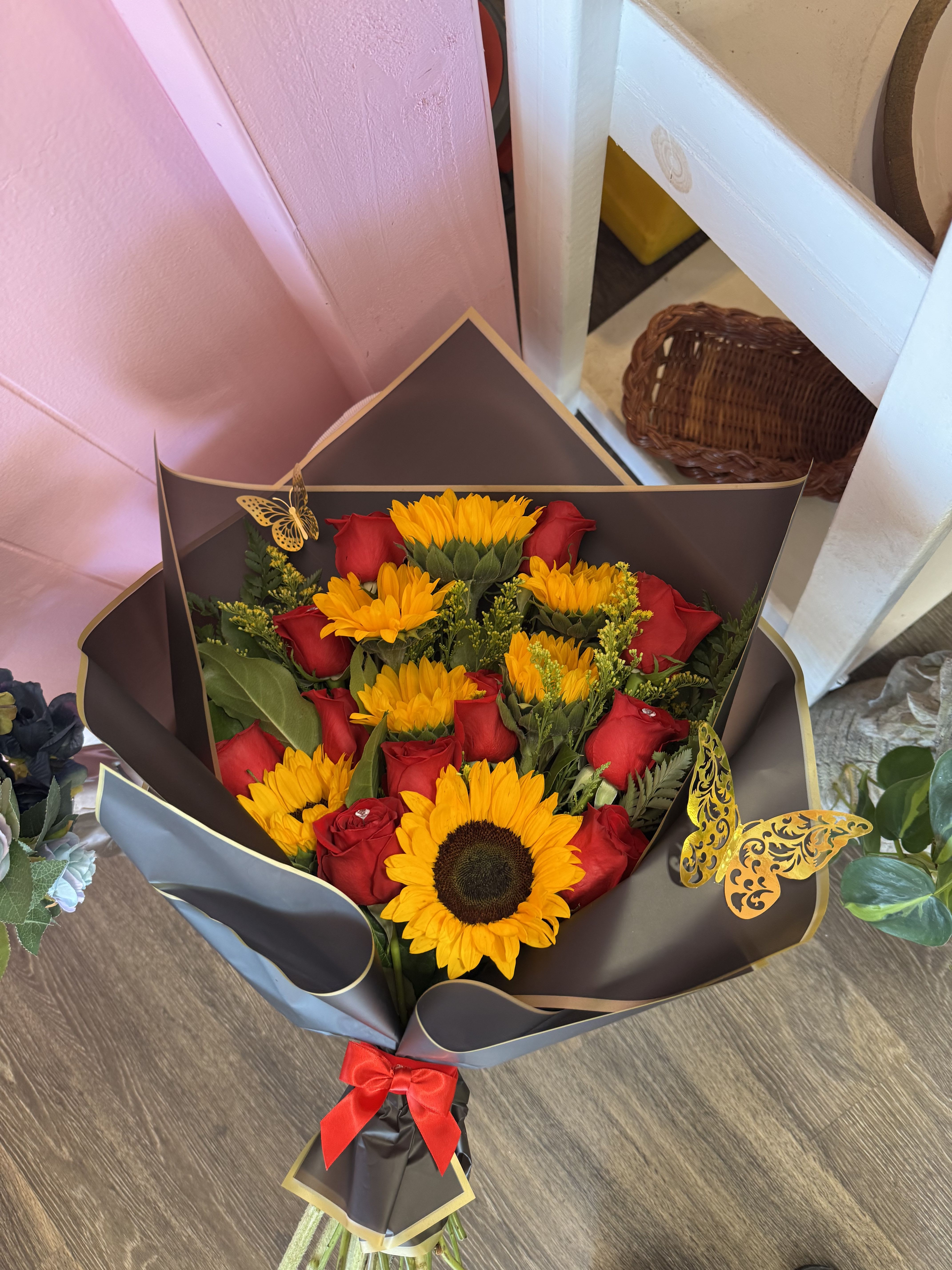 Bouquet of red roses and yellow sunflowers wrapped in dark paper