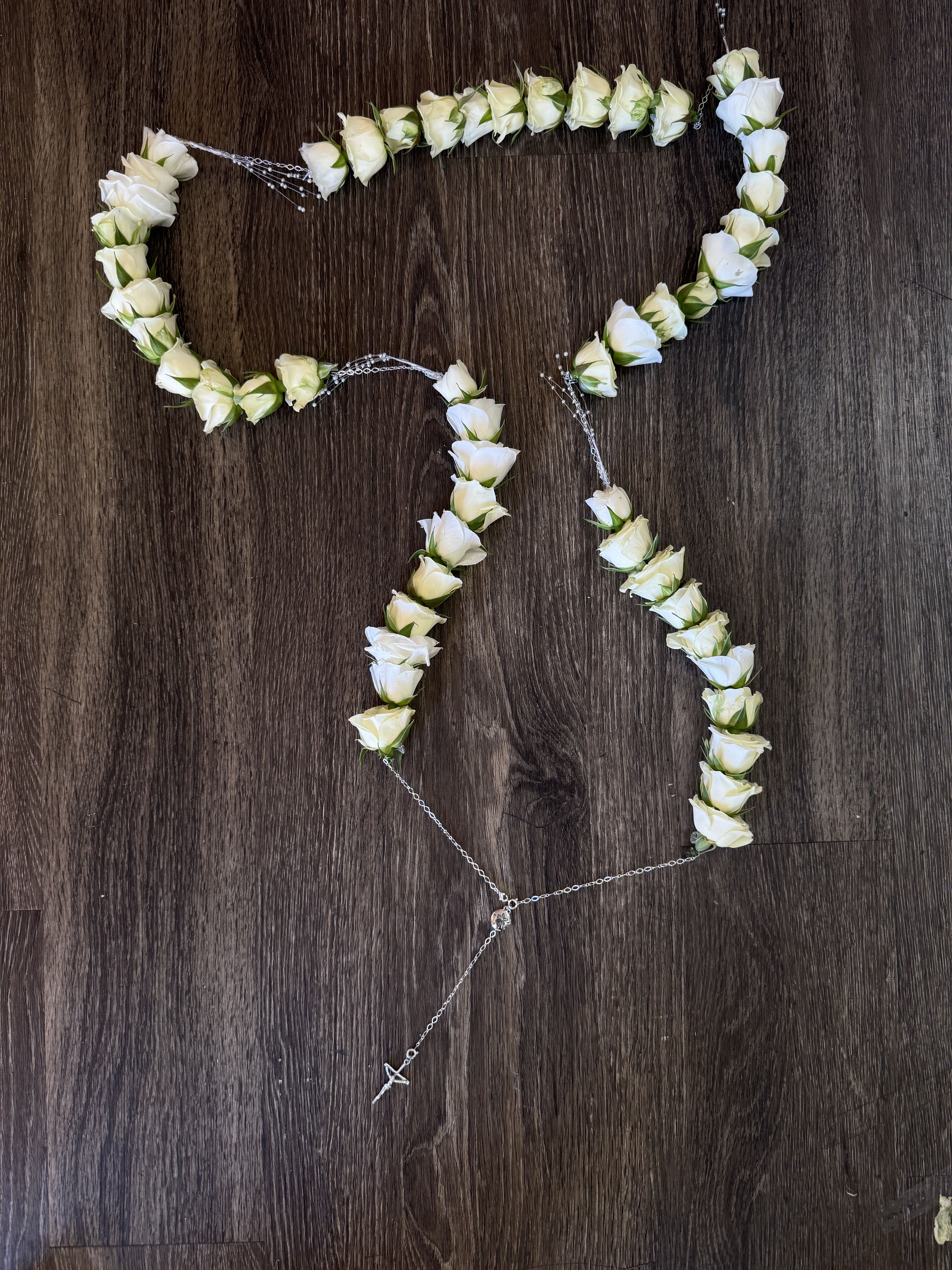 White rose floral garland arranged in a looping shape on a dark wood surface