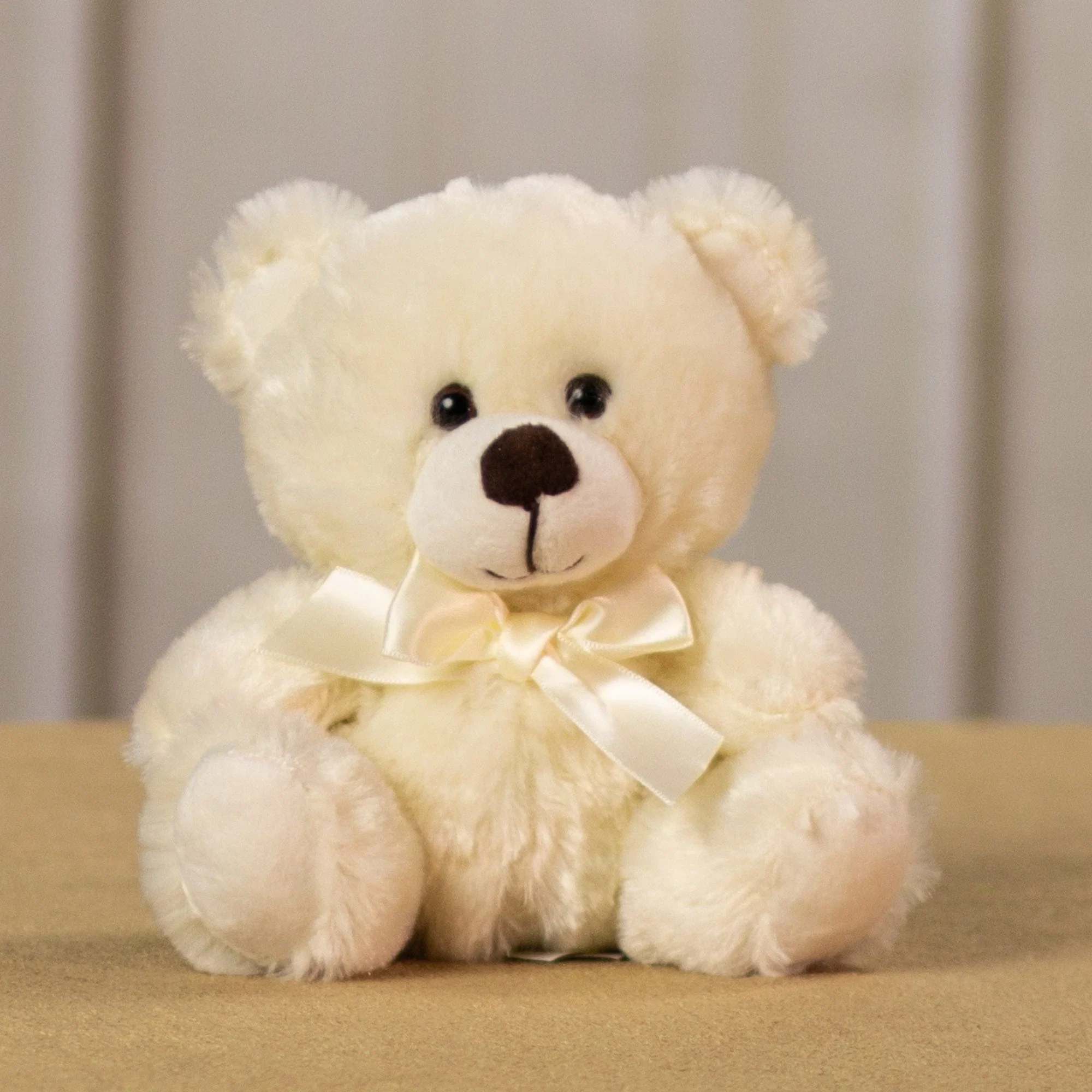 Cream teddy bear with a satin bow sitting on a tan surface