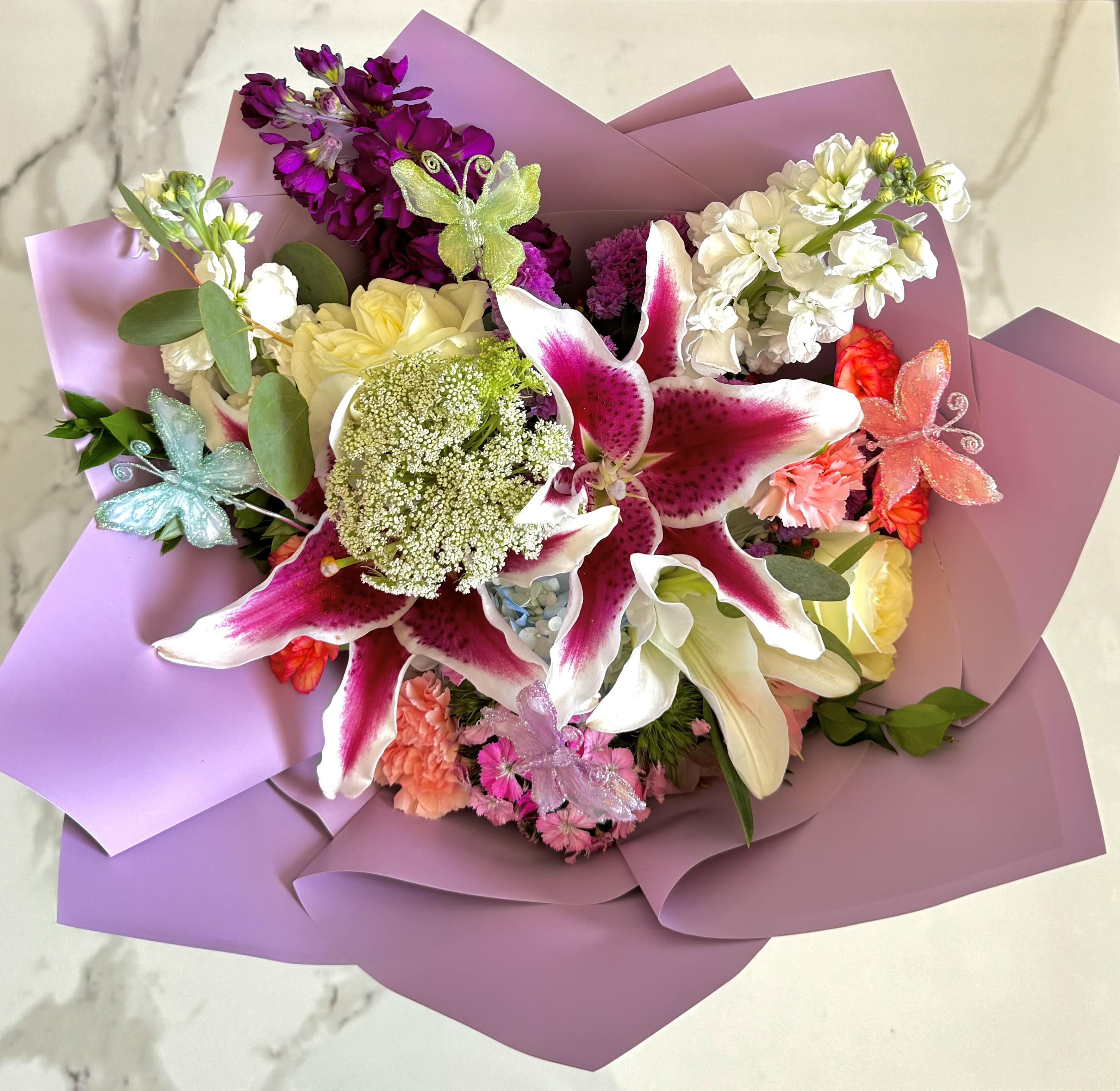 Bouquet of pink lilies, white roses, and purple flowers wrapped in lavender paper