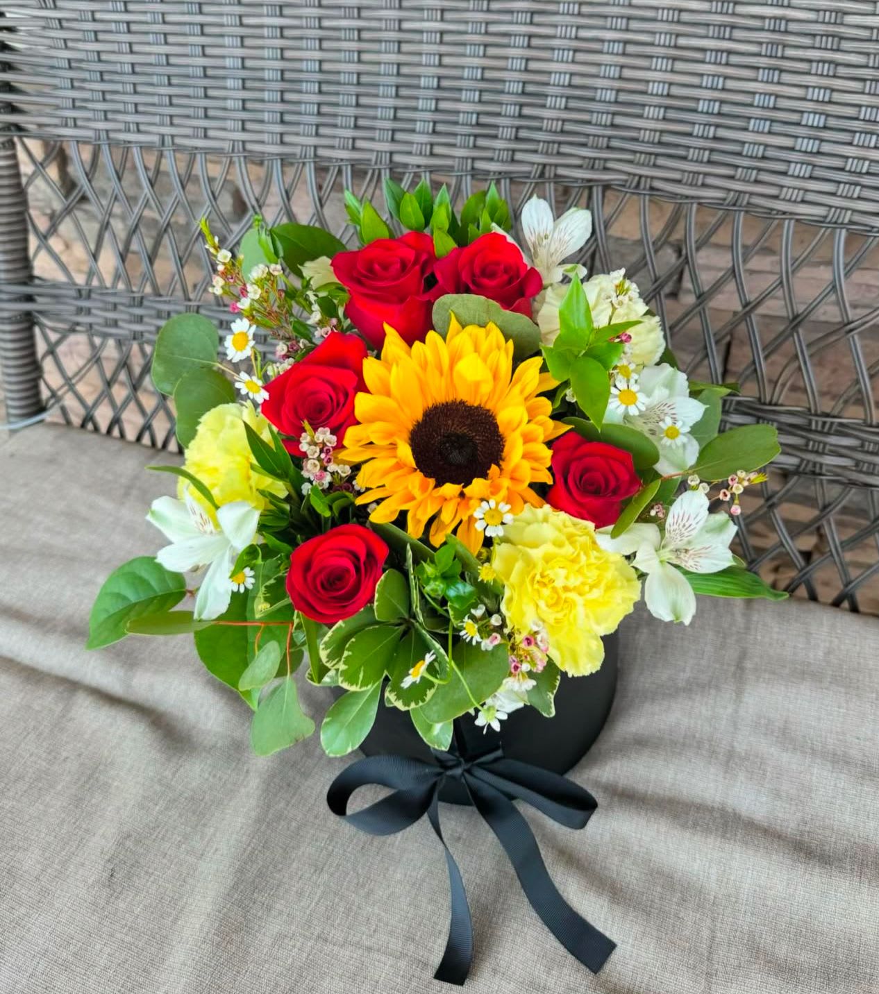Bouquet of red roses, a sunflower, and yellow carnations in a black box