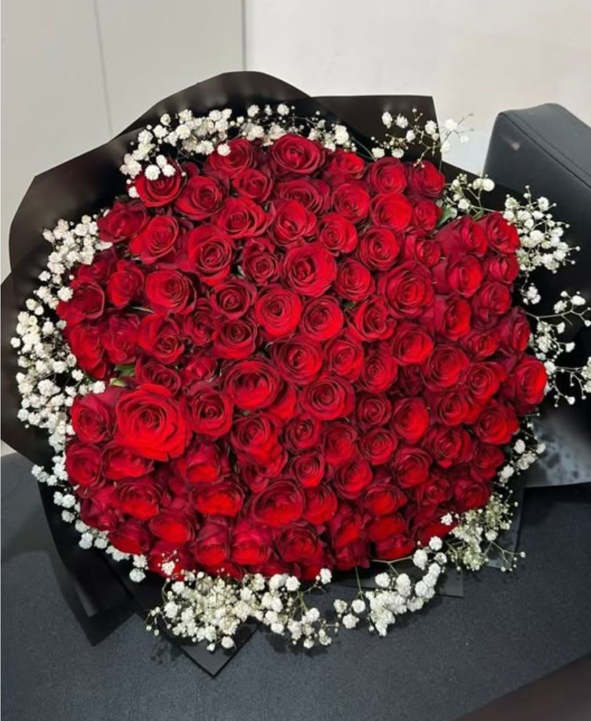 Large bouquet of red roses with white baby's breath in black wrap